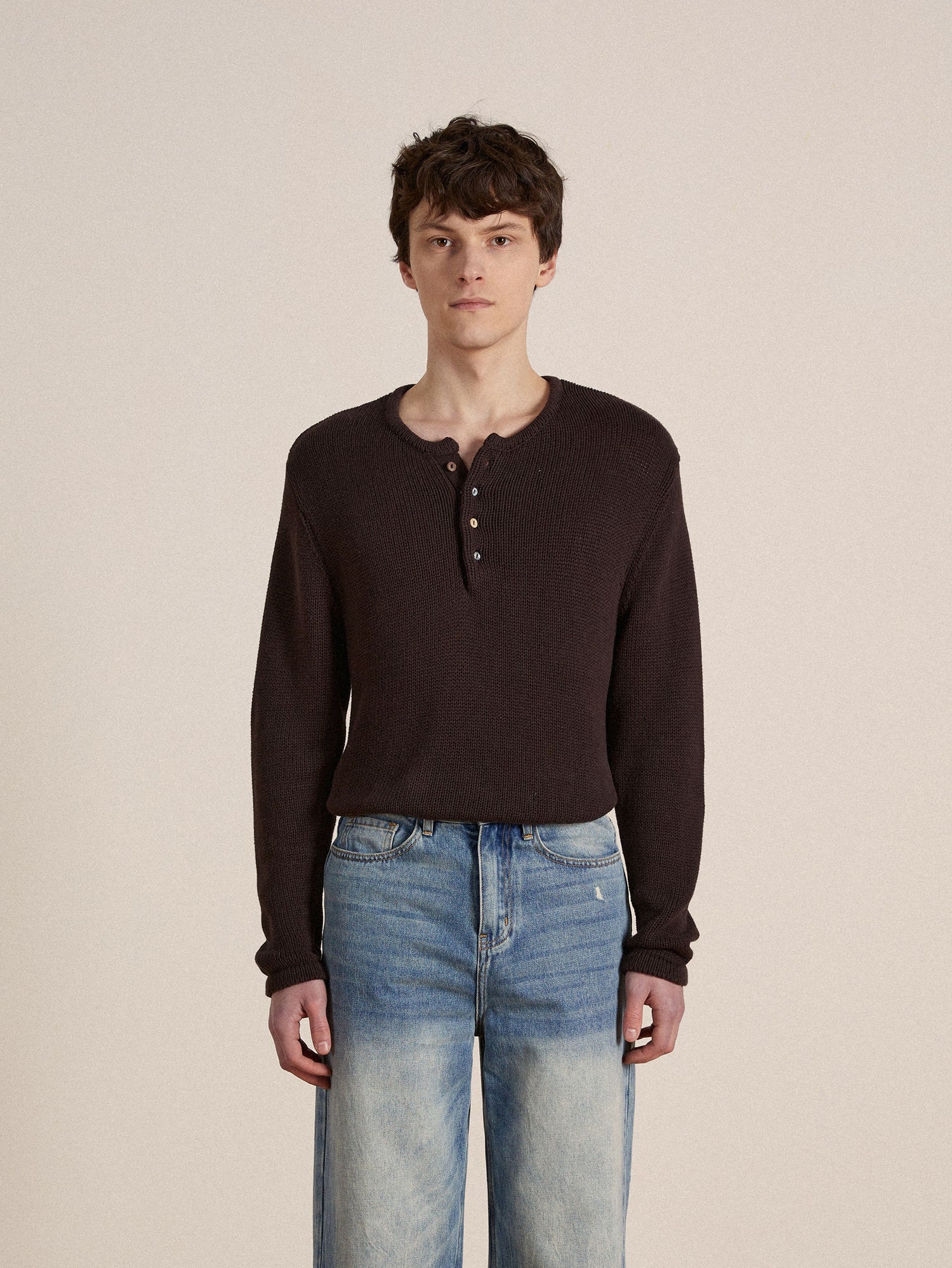 A man wearing a brown Profound knit Henley sweater and blue jeans.