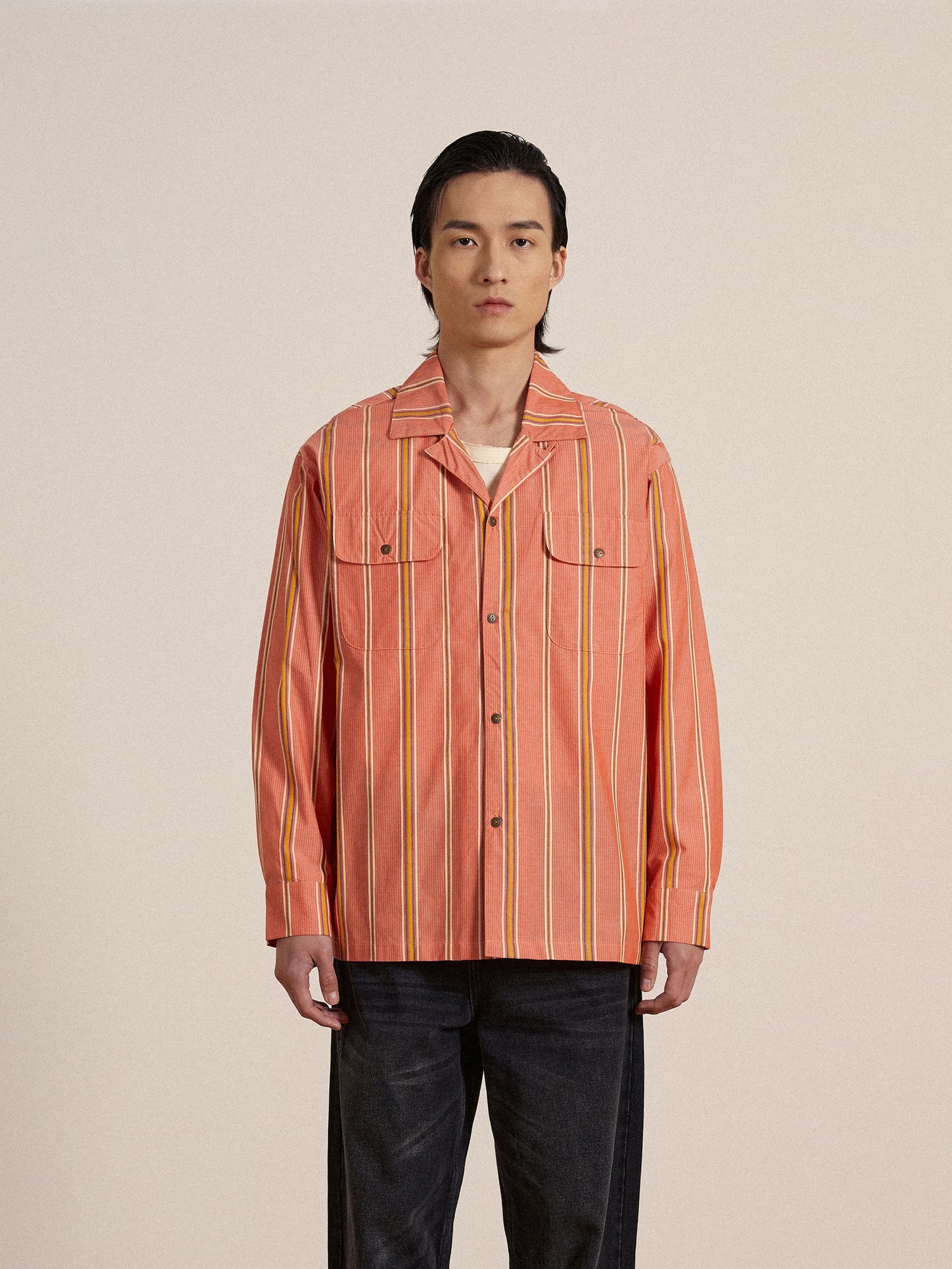 A man wearing an orange Found Stripe Citrus LS Camp Shirt and jeans.