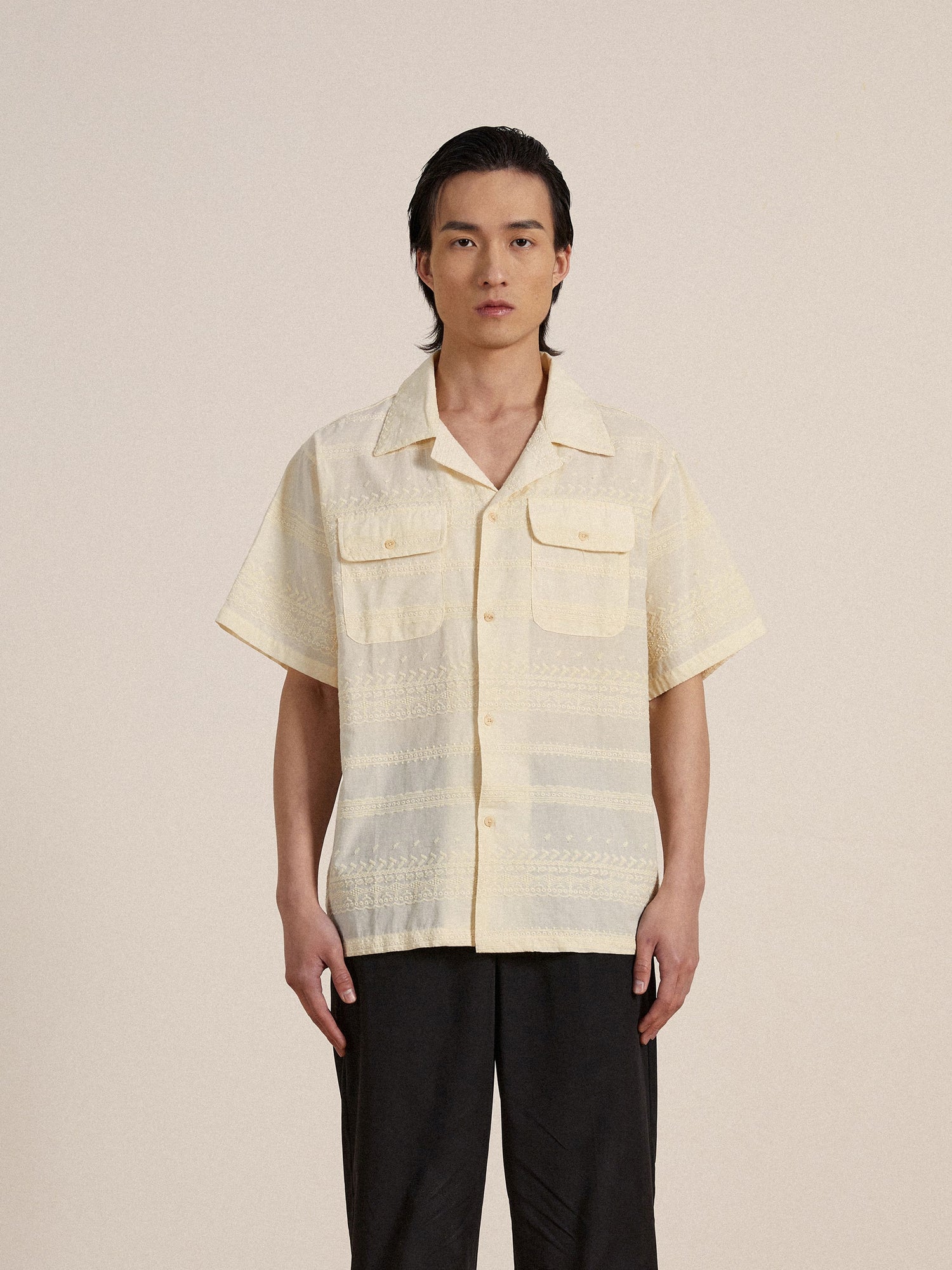 A man wearing a yellow Found Lace SS Camp Shirt with delicate lace detailing and black pants.