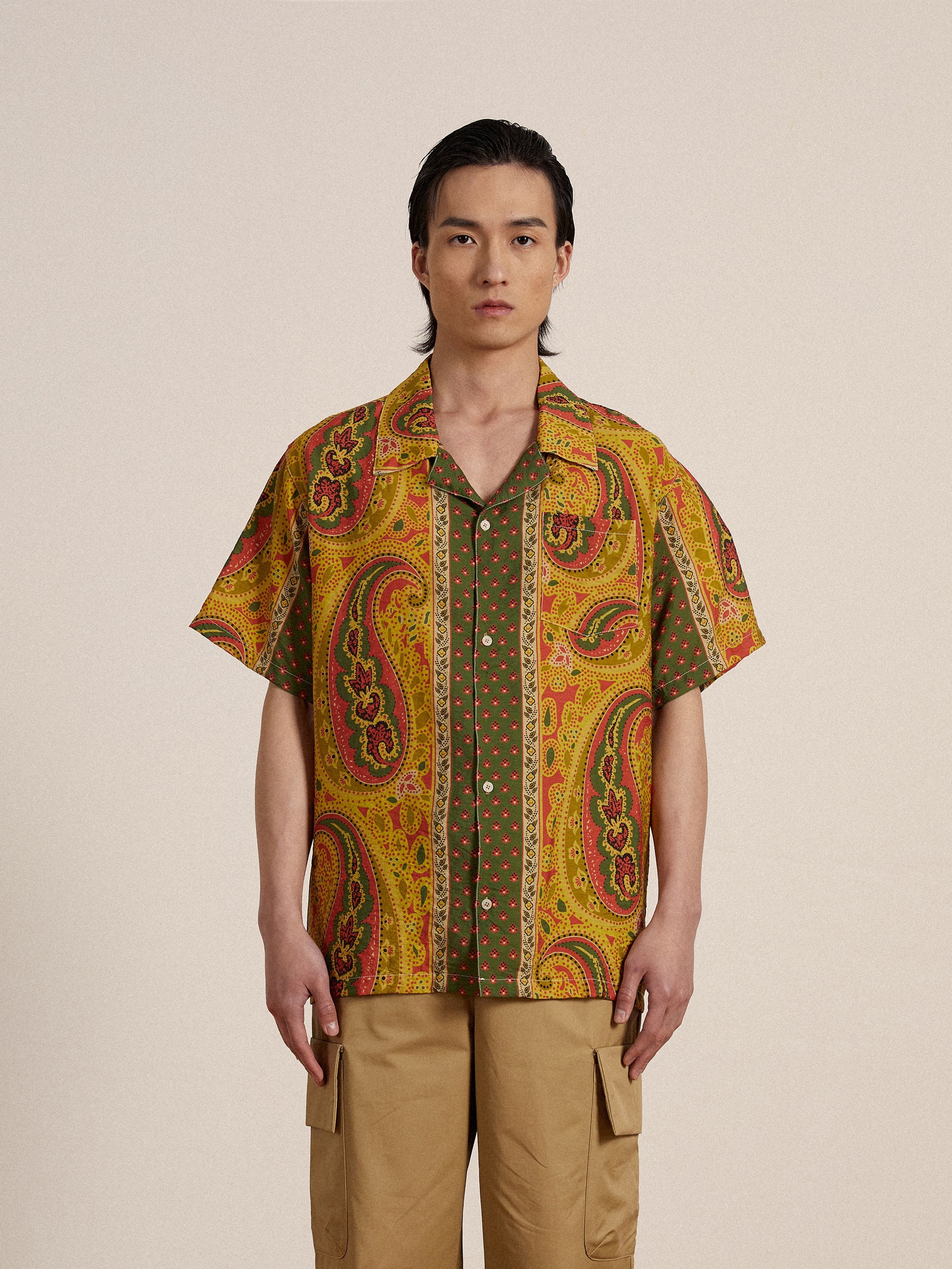 A man wearing a yellow Found Pench Paisley SS Camp Shirt and khaki pants.