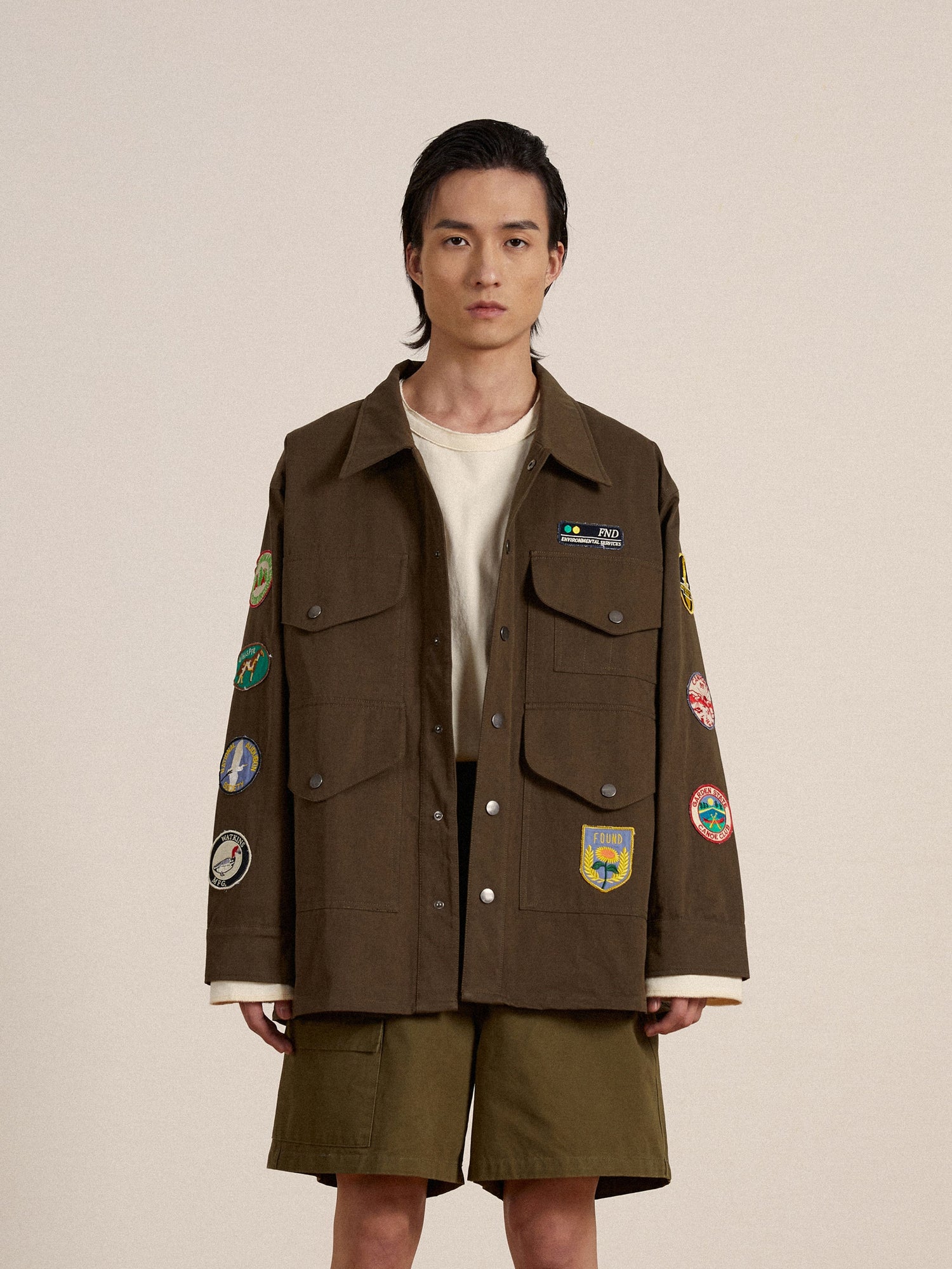 A man wearing a brown Found Multi Patch Work Jacket with embroidered patches on it.