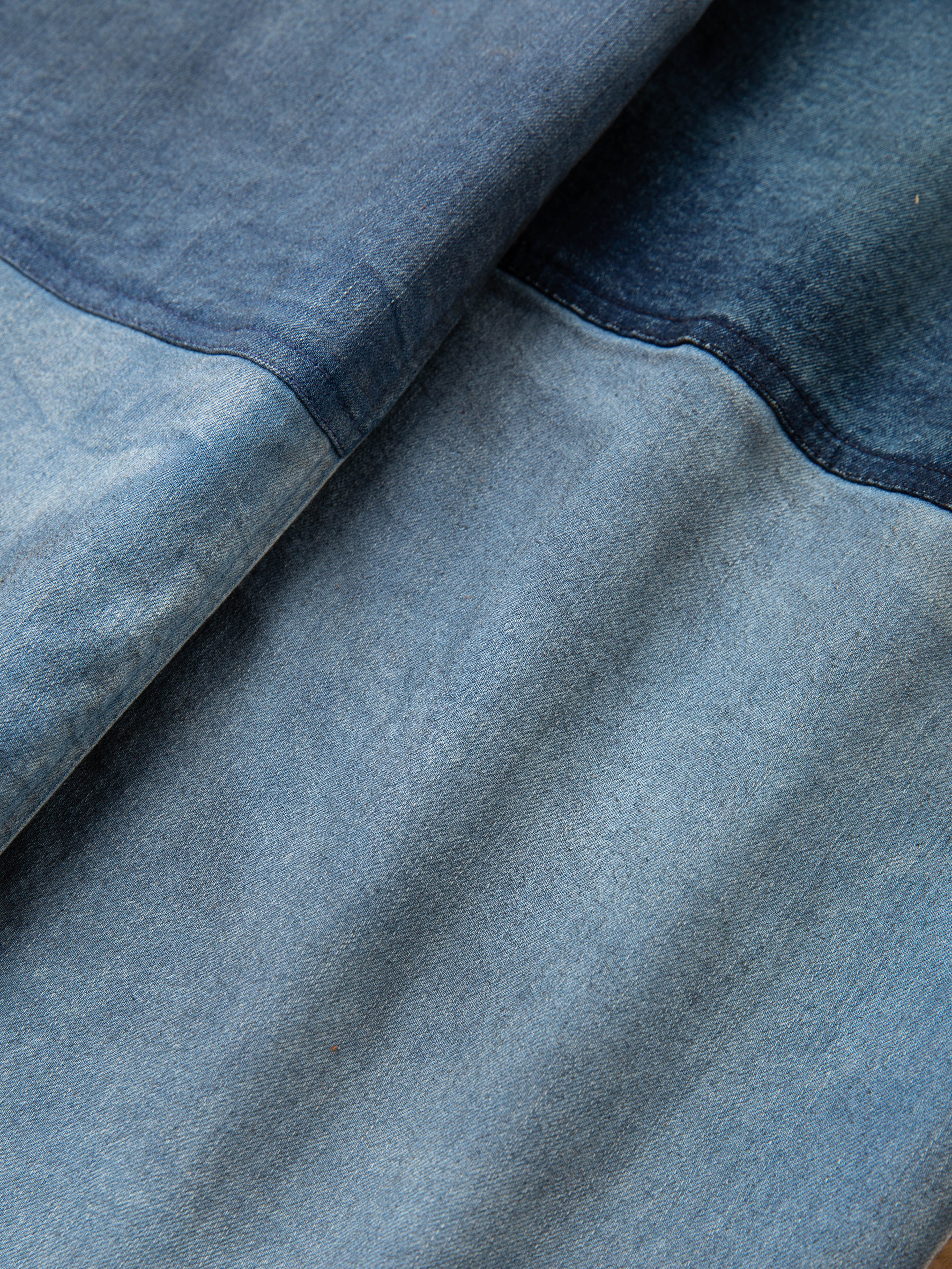 Close-up of the FOUND Multi Patch Painters Work Pants fabric with different shades of blue. The texture and seams are visible, reminiscent of antique French painter uniforms, showcasing distinct sections of lighter and darker blue areas.