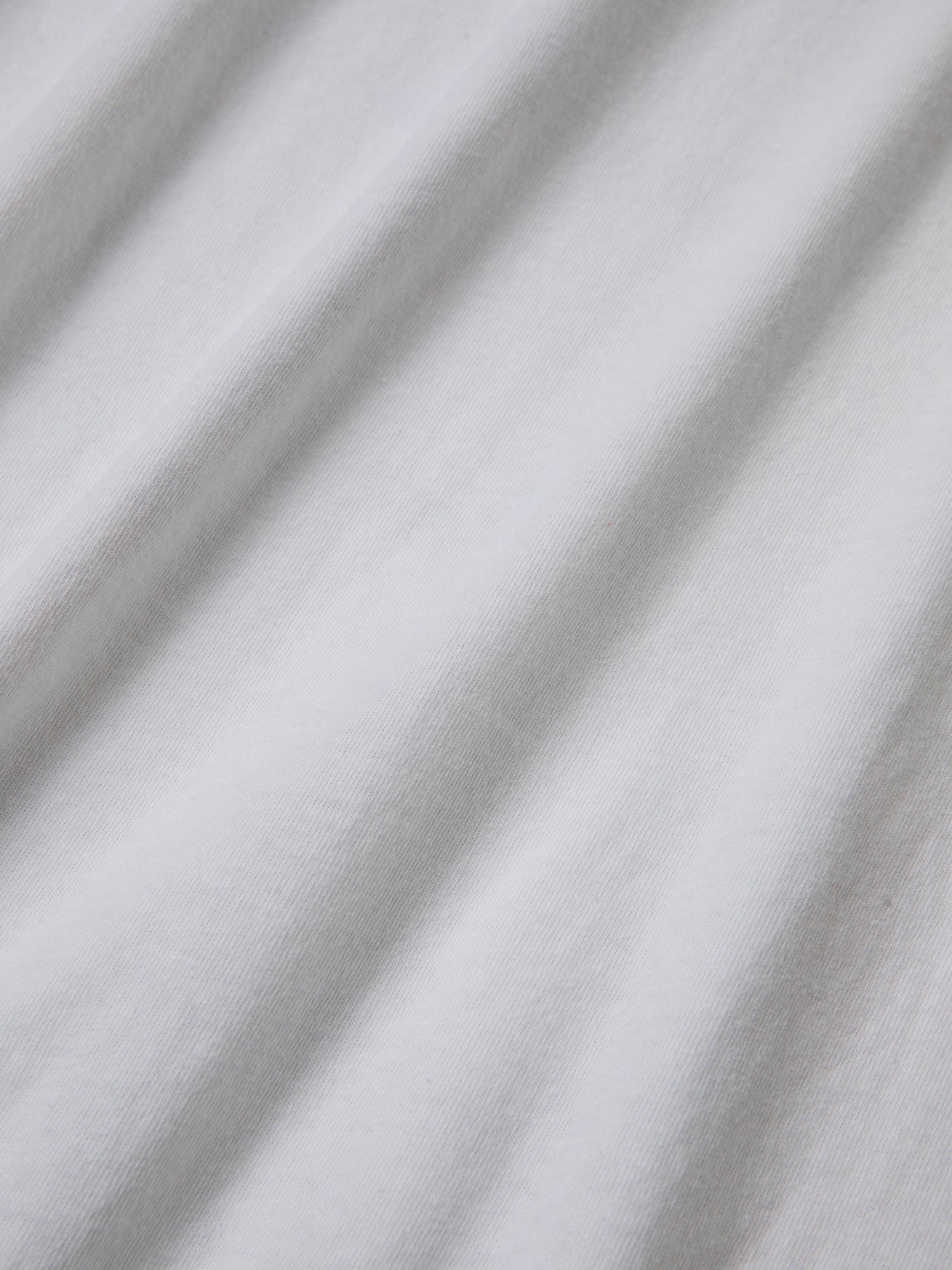 Close-up of white 100% cotton fabric with visible texture and subtle shadowing from folds, reminiscent of the classic Malibu Farm Fair Tee by FOUND.