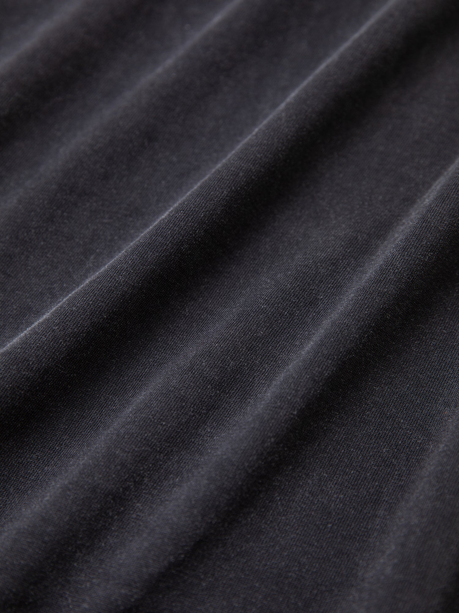 Close-up of a dark grey fabric with visible folds and a smooth texture, highlighting the quality of the 100% cotton Horse Logo Print Tee by FOUND, treated with an enzyme wash for exceptional softness.