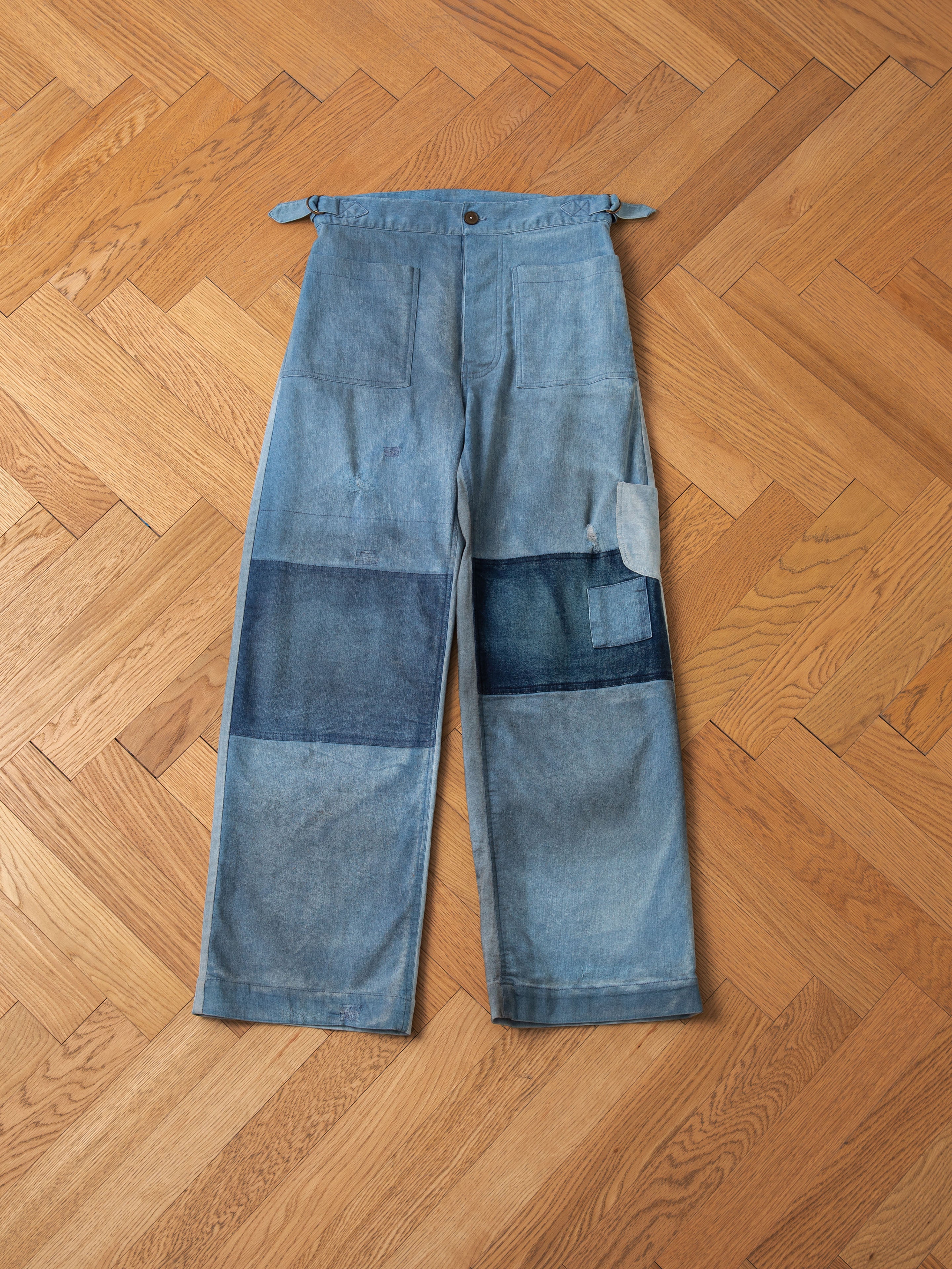 A pair of blue FOUND Multi Patch Painters Work Pants with a classic slouchy fit, lying flat on a herringbone wood floor.