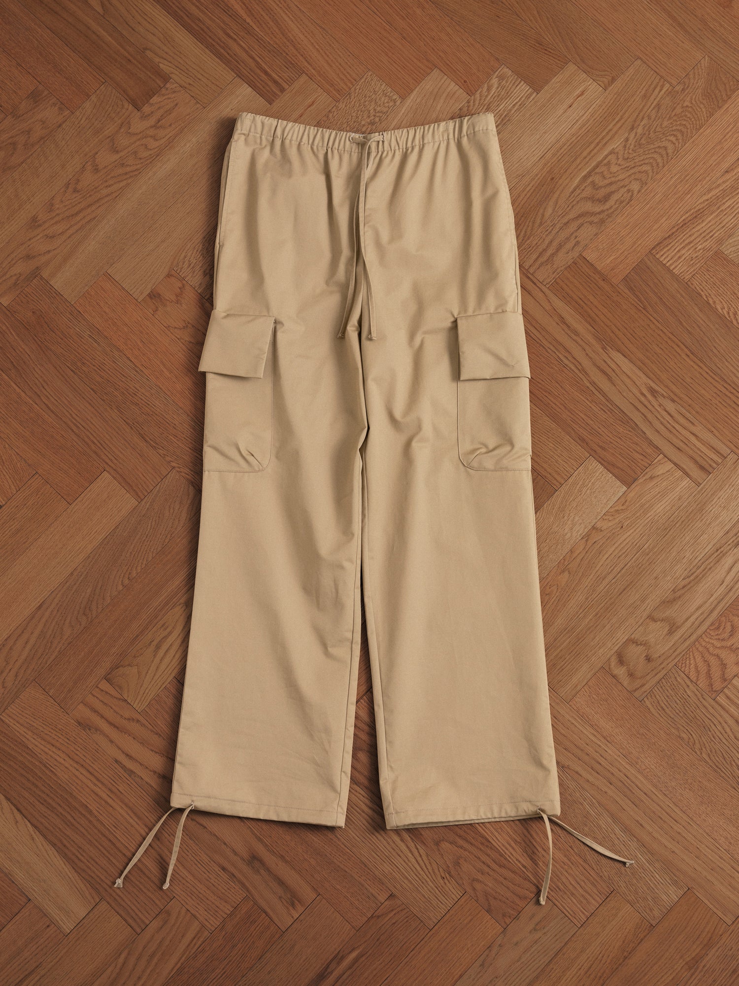 A pair of Found Twill Cargo Drawstring Pants in tan on a wooden floor.