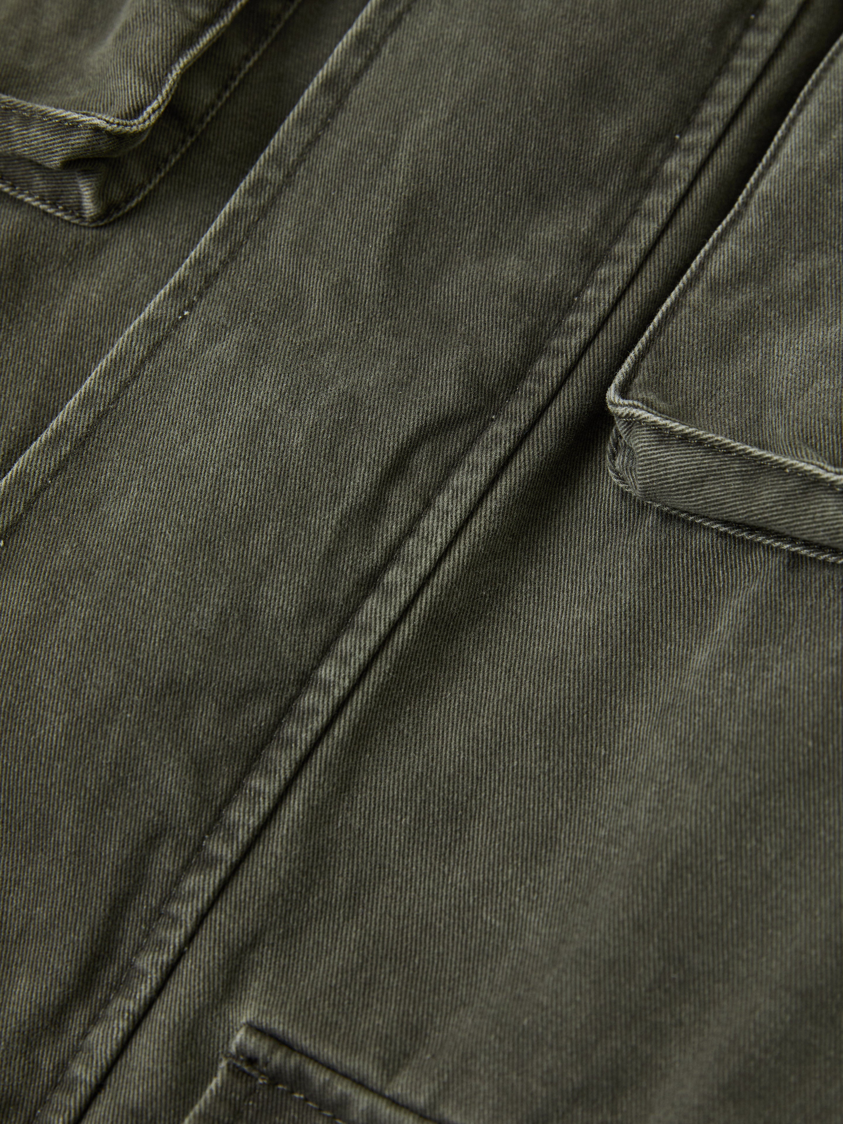 A close-up of the dark green M65 Utility Twill Pocket Jacket by FOUND, showcasing visible seams and two flap pockets that capture the essence of military-inspired outerwear.