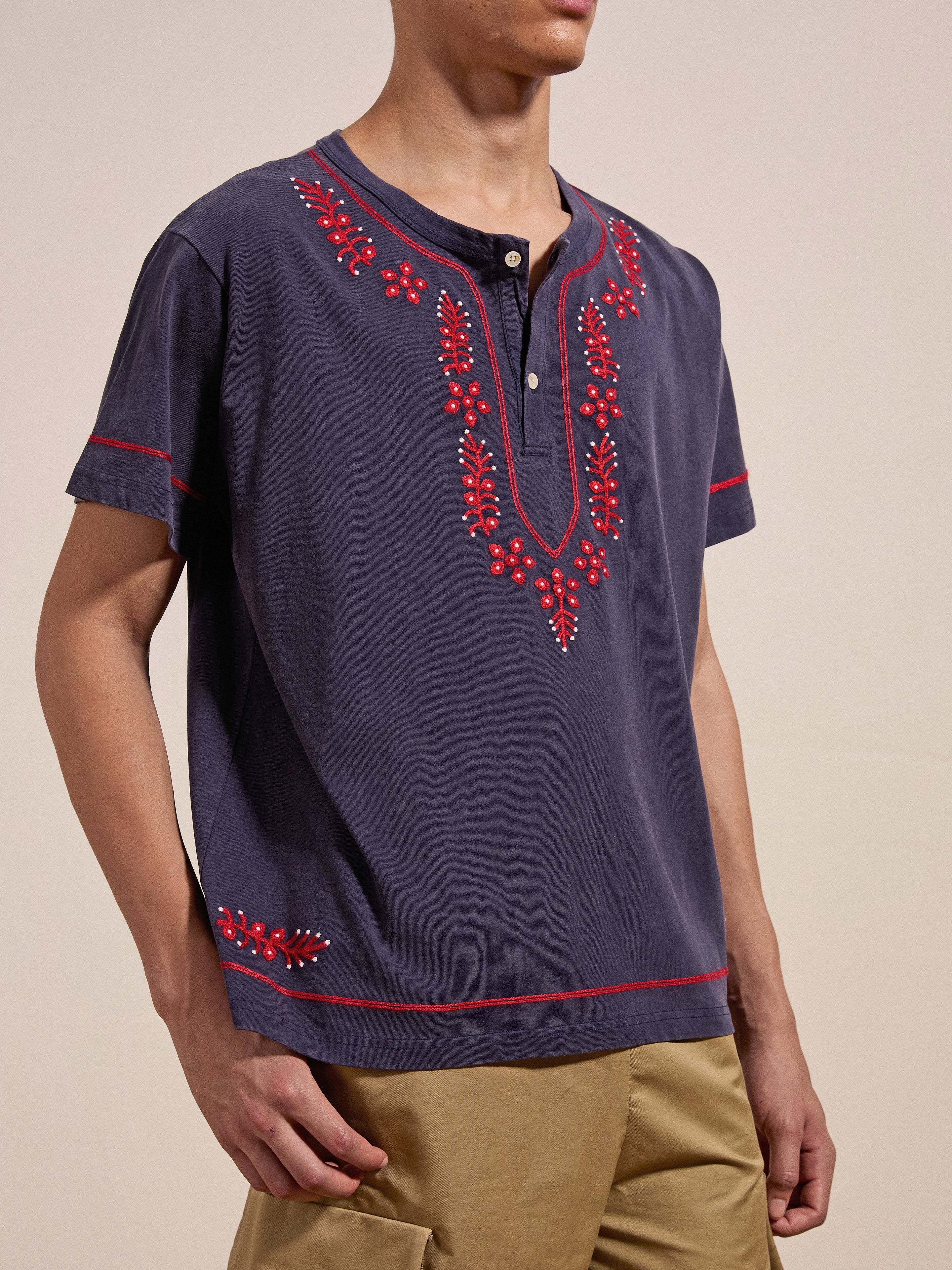 A person is wearing a dark blue Embroidered Henley by FOUND with red floral designs and beige pants.