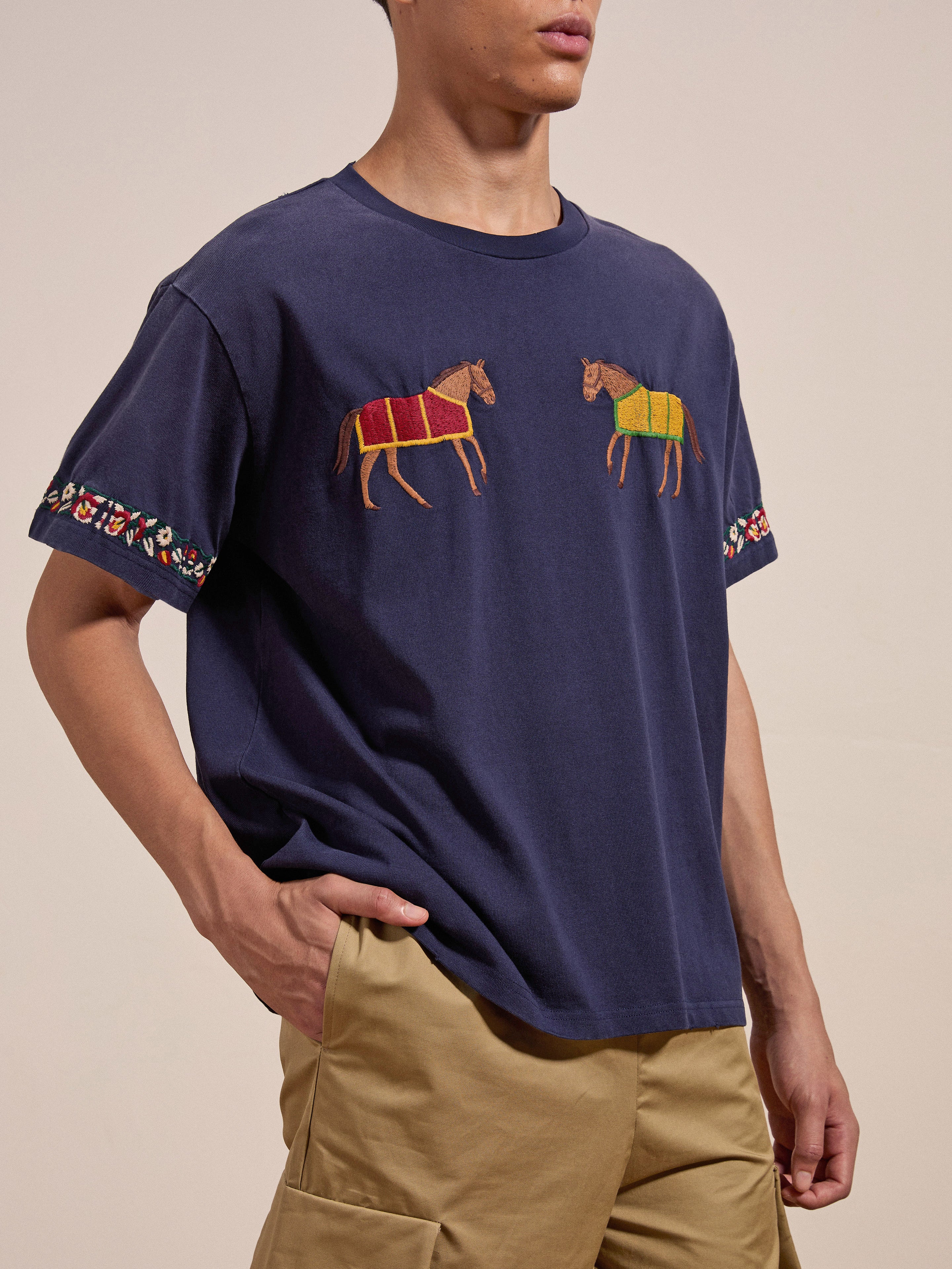 A person wearing the FOUND Horse Equine Tee, showcasing navy blue fabric with horse designs on the chest and vibrant embroidered patterns on the sleeves, paired with khaki pants.