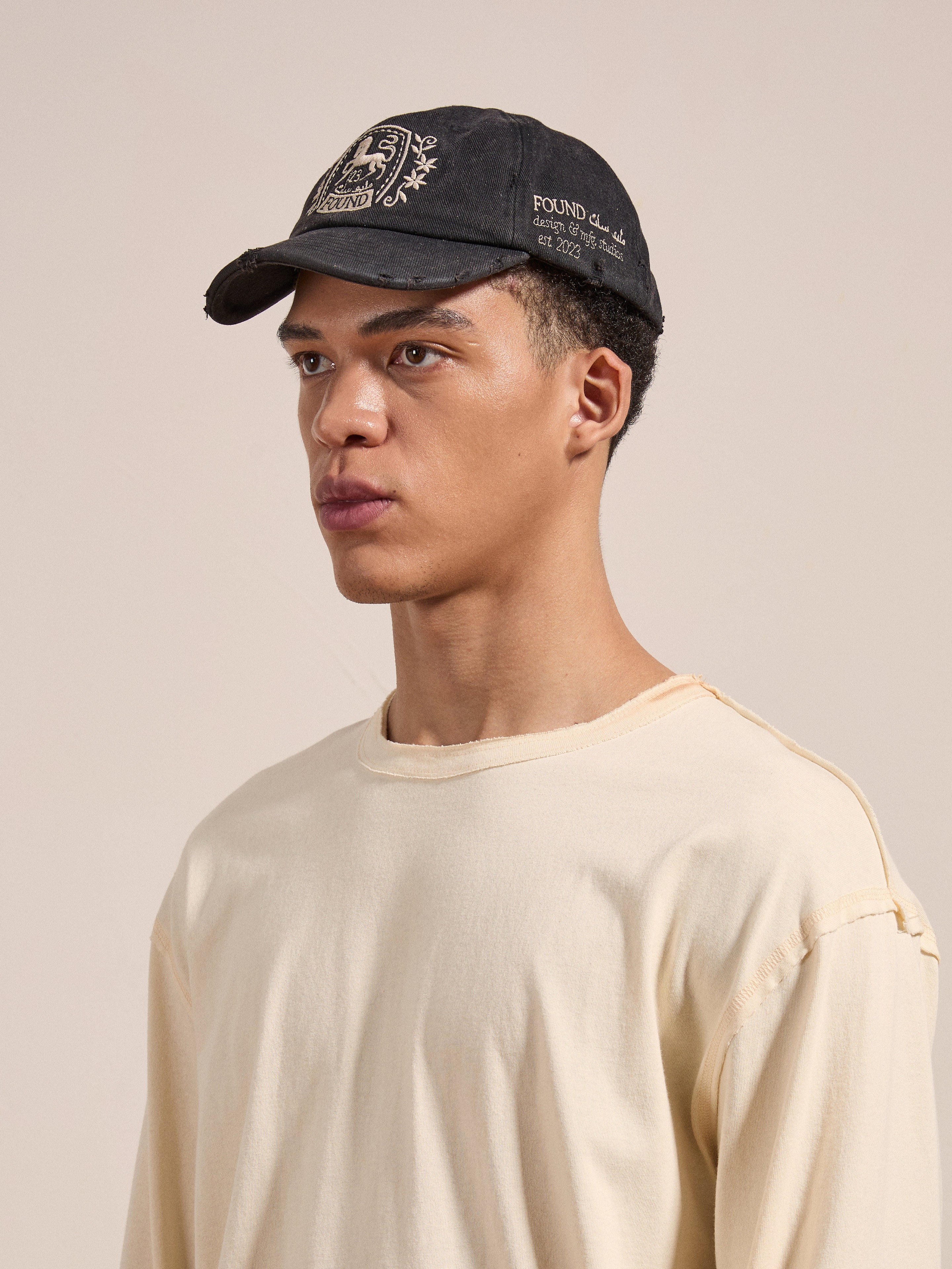 A person wearing a beige long-sleeve shirt and FOUND's Logo Crest Cap stands against a plain background.