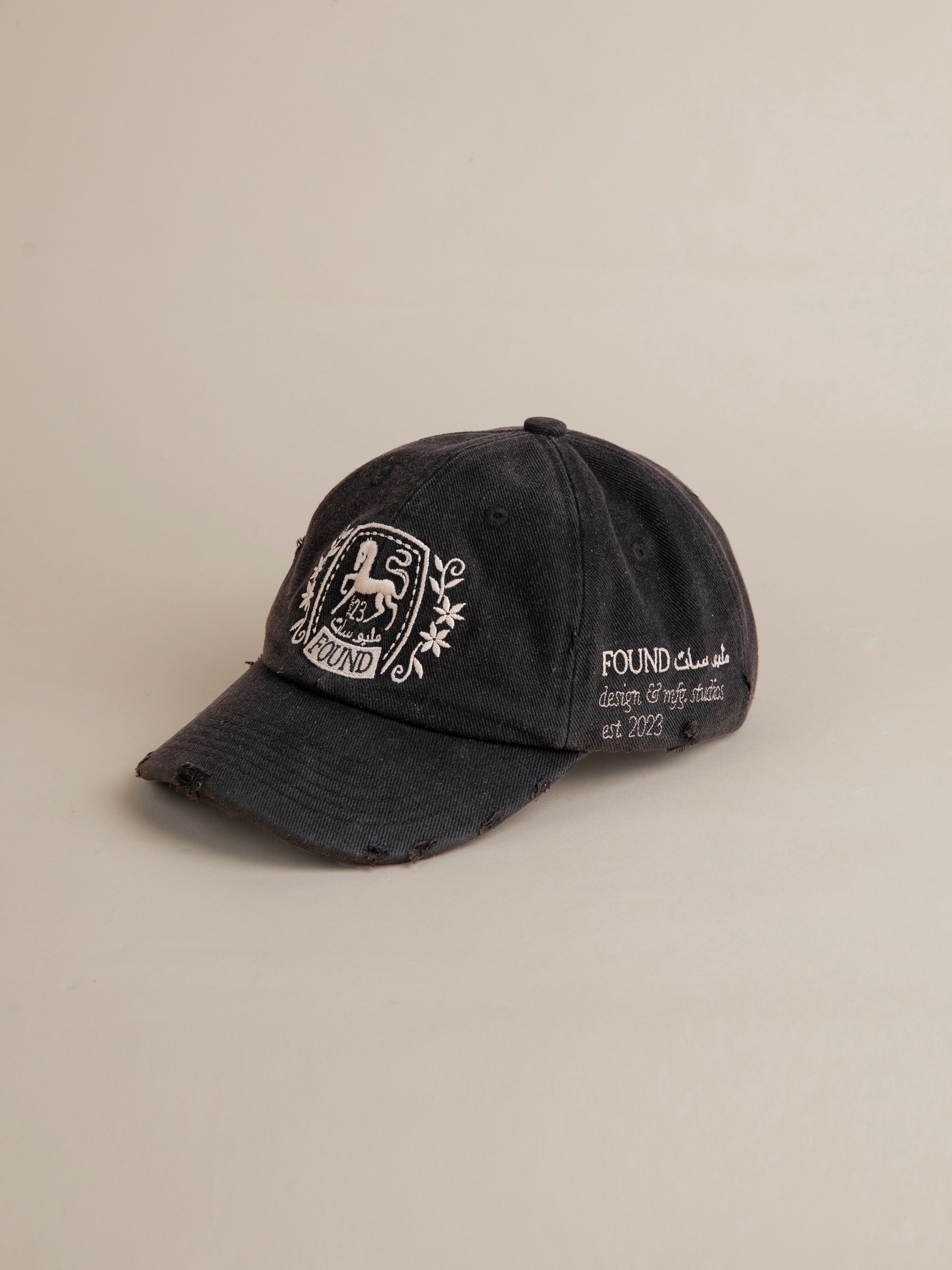 FOUND's Logo Crest Cap is a black baseball cap featuring an embroidered horse logo combined with a hand motif and the text "FOUND design & craft studio est. 2023." This cap expertly incorporates traditional South Asian motifs into its design.