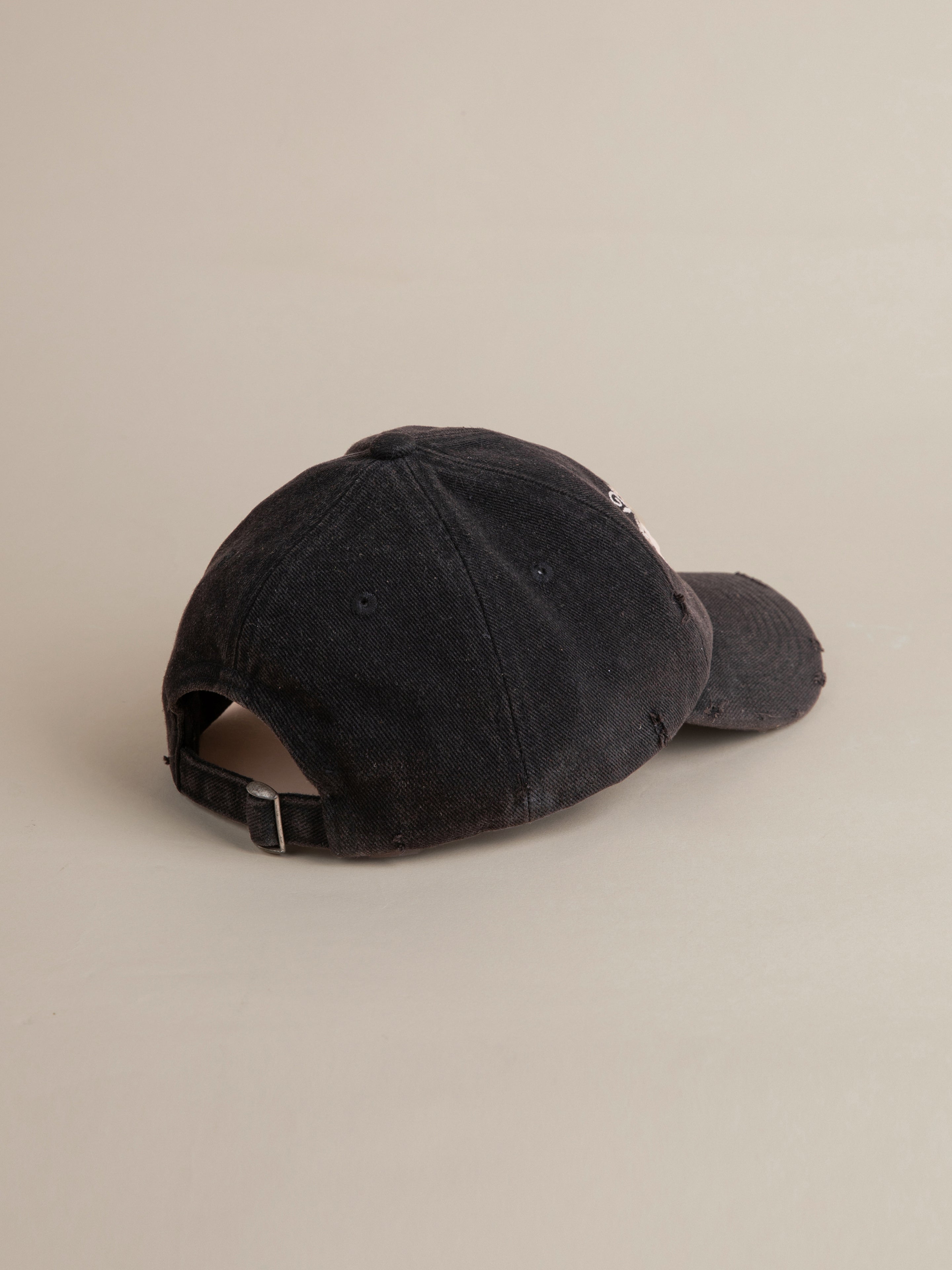 A black, worn FOUND Logo Crest Cap lies upside down on a beige surface, revealing its adjustable strap and back opening adorned with an embroidered horse logo.