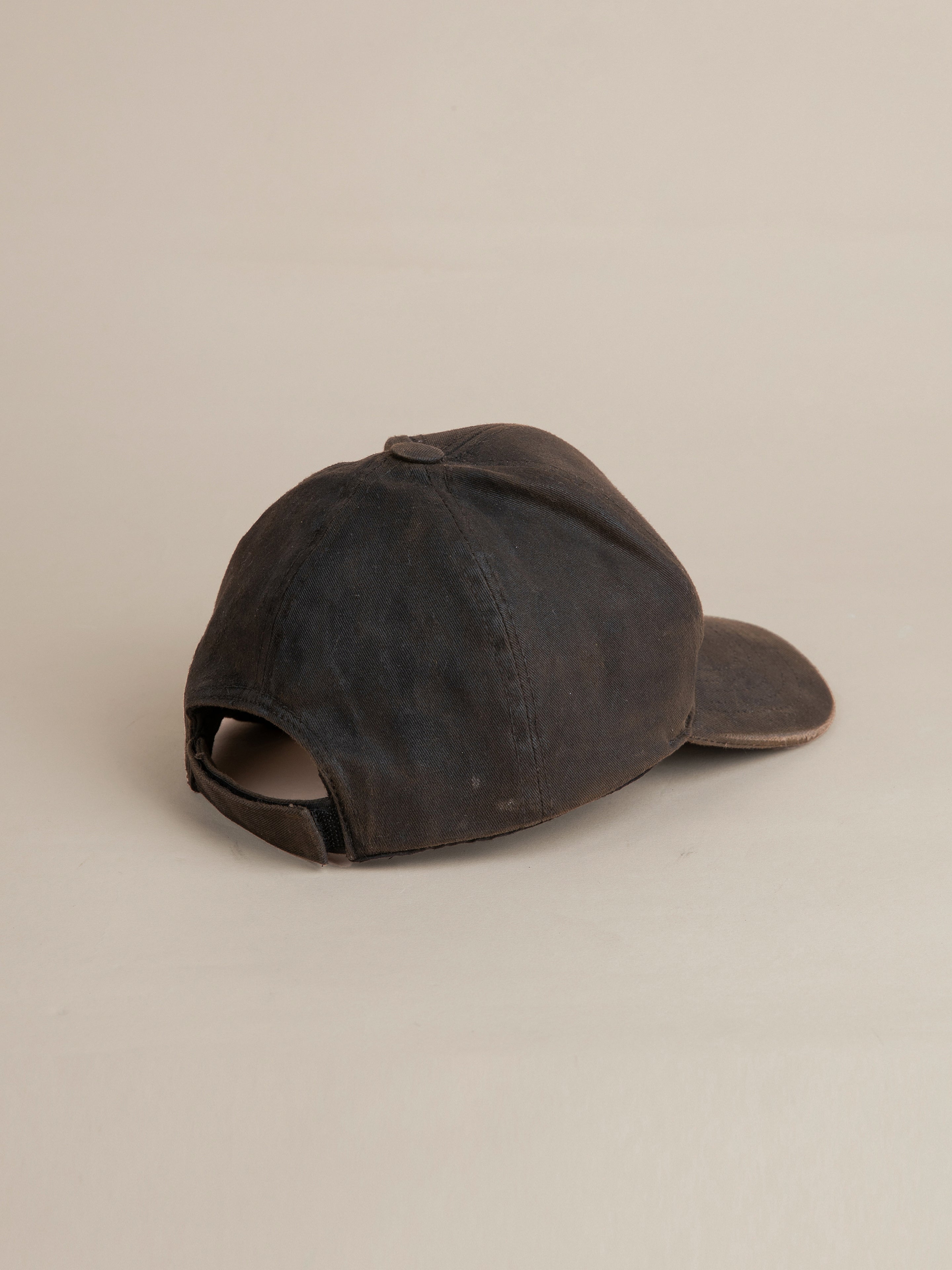 A worn Waxed Charcoal Studded Cap by FOUND, shown from the back, displaying an adjustable strap and a slightly curved brim on a neutral background.