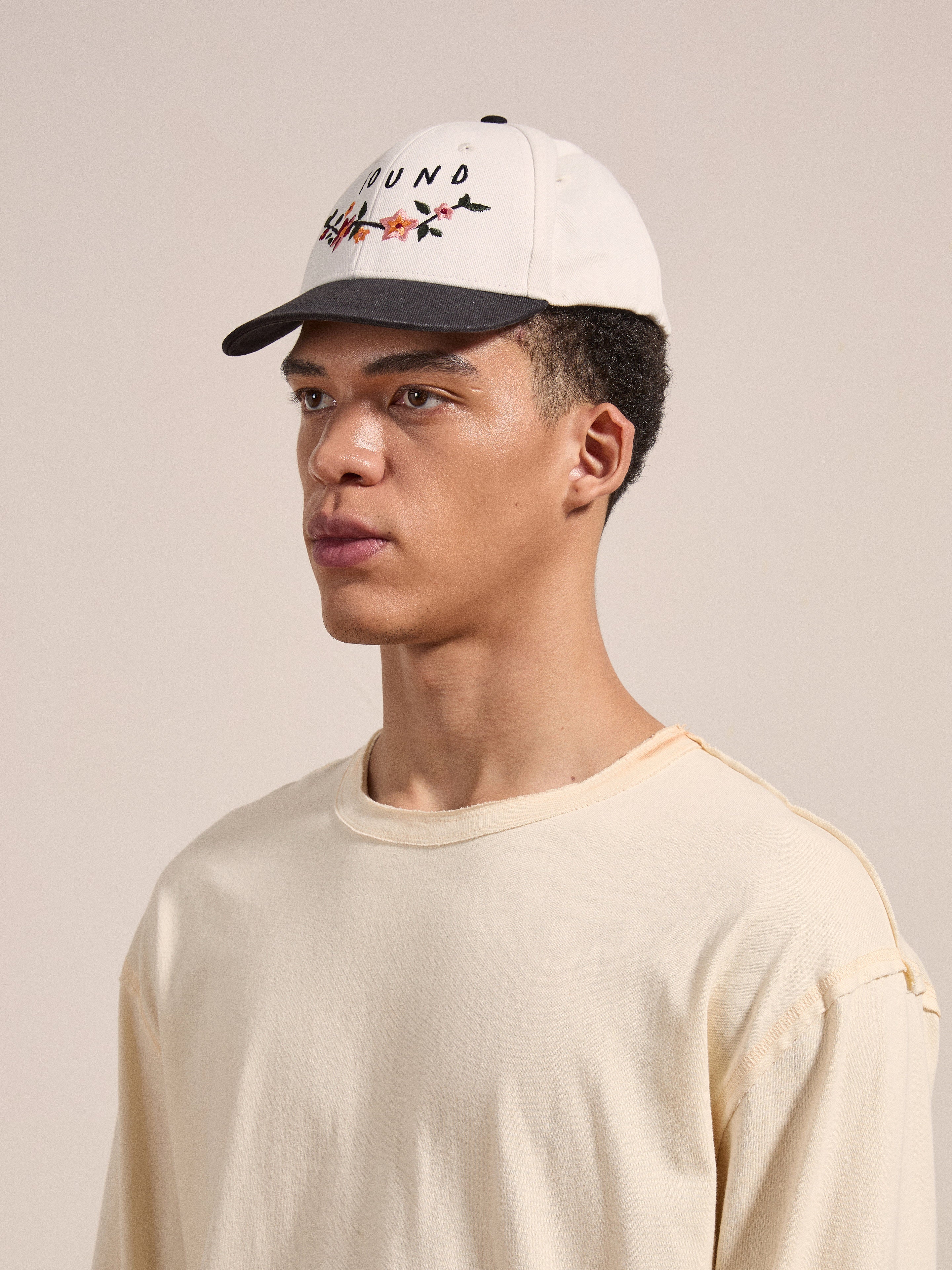 A person wearing a beige long-sleeve shirt and FOUND's Greenlands Contrast Cap, featuring colorful text and designs, looks off-camera against a plain background.