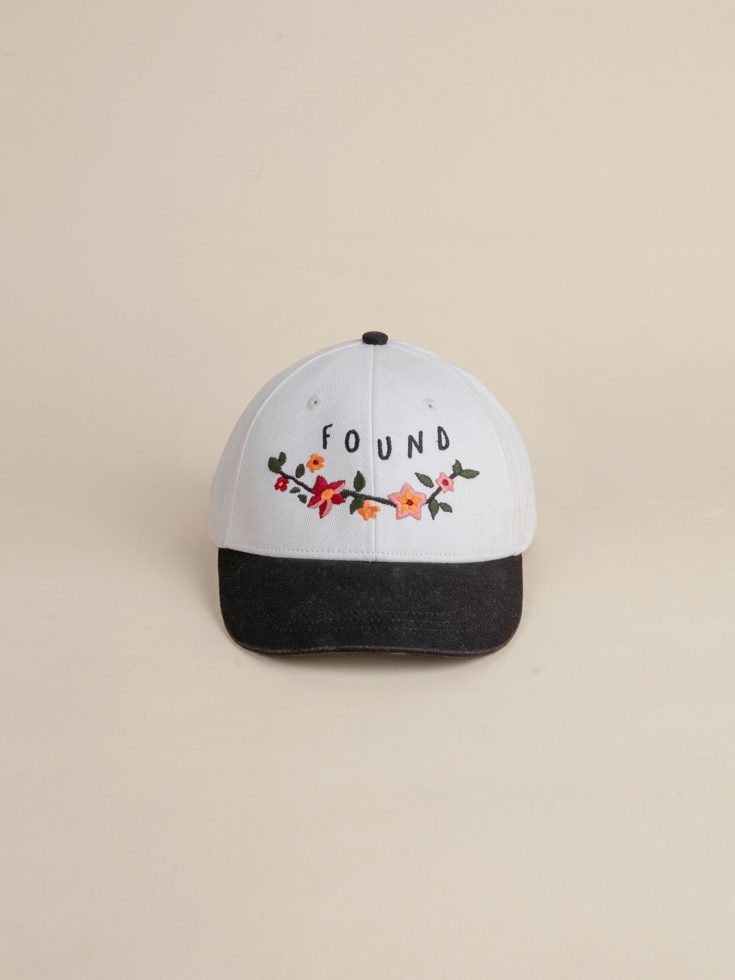 The Greenlands Contrast Cap by FOUND is a white 6-panel curved brim baseball cap, accentuated with a black brim, showcasing Kantha-style floral embroidery and the word 