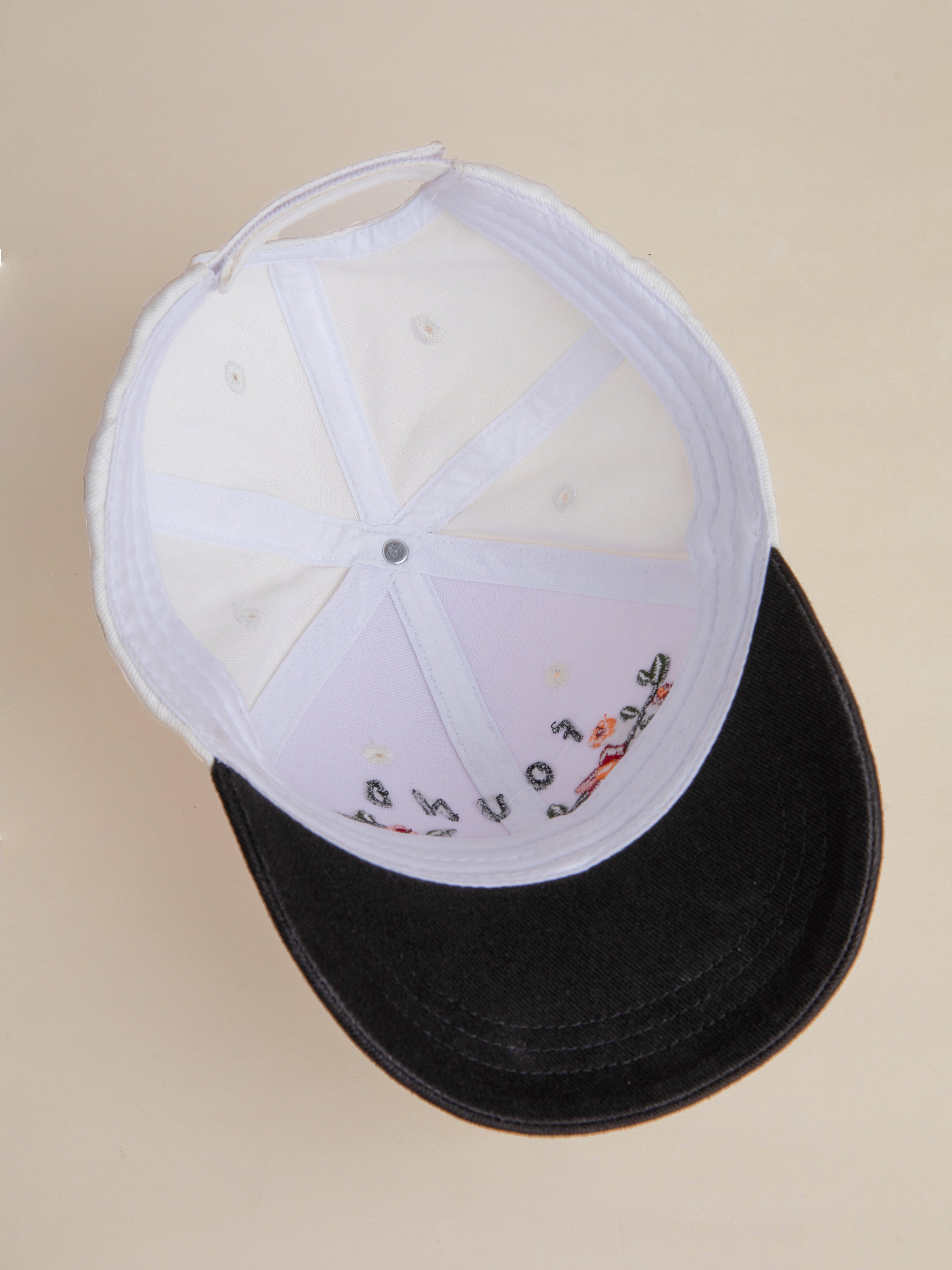 An upside-down black and white Greenlands Contrast Cap by FOUND, showcasing the interior stitching, labels, and adjustable strap.