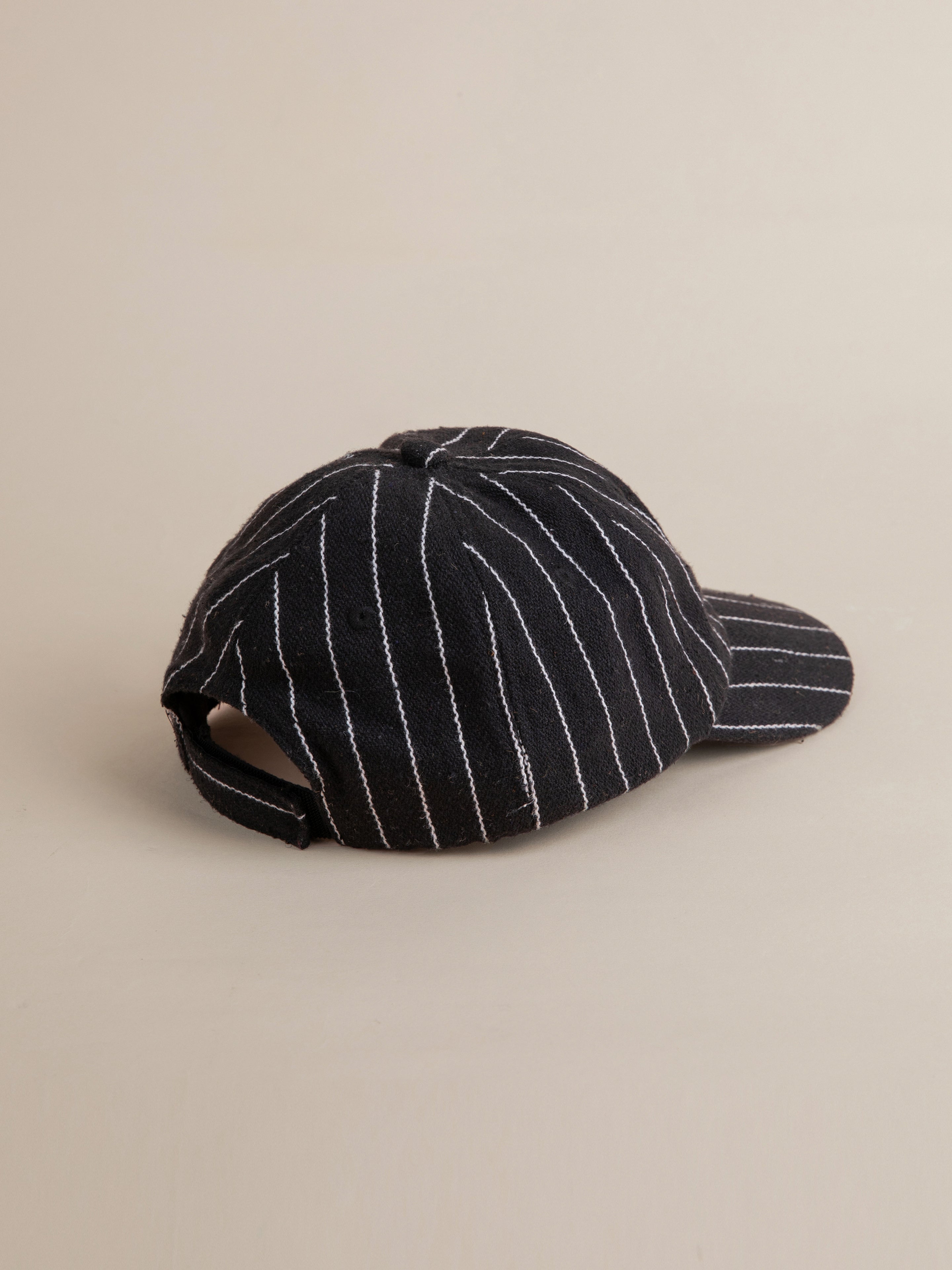 The FOUND Pinstripe Lion Cap features classic black and white vertical pinstripes, highlighted by a view from the back to showcase its adjustable strap. This stylish baseball cap also boasts an embroidered lion logo on the front, blending modernity with timeless elegance.