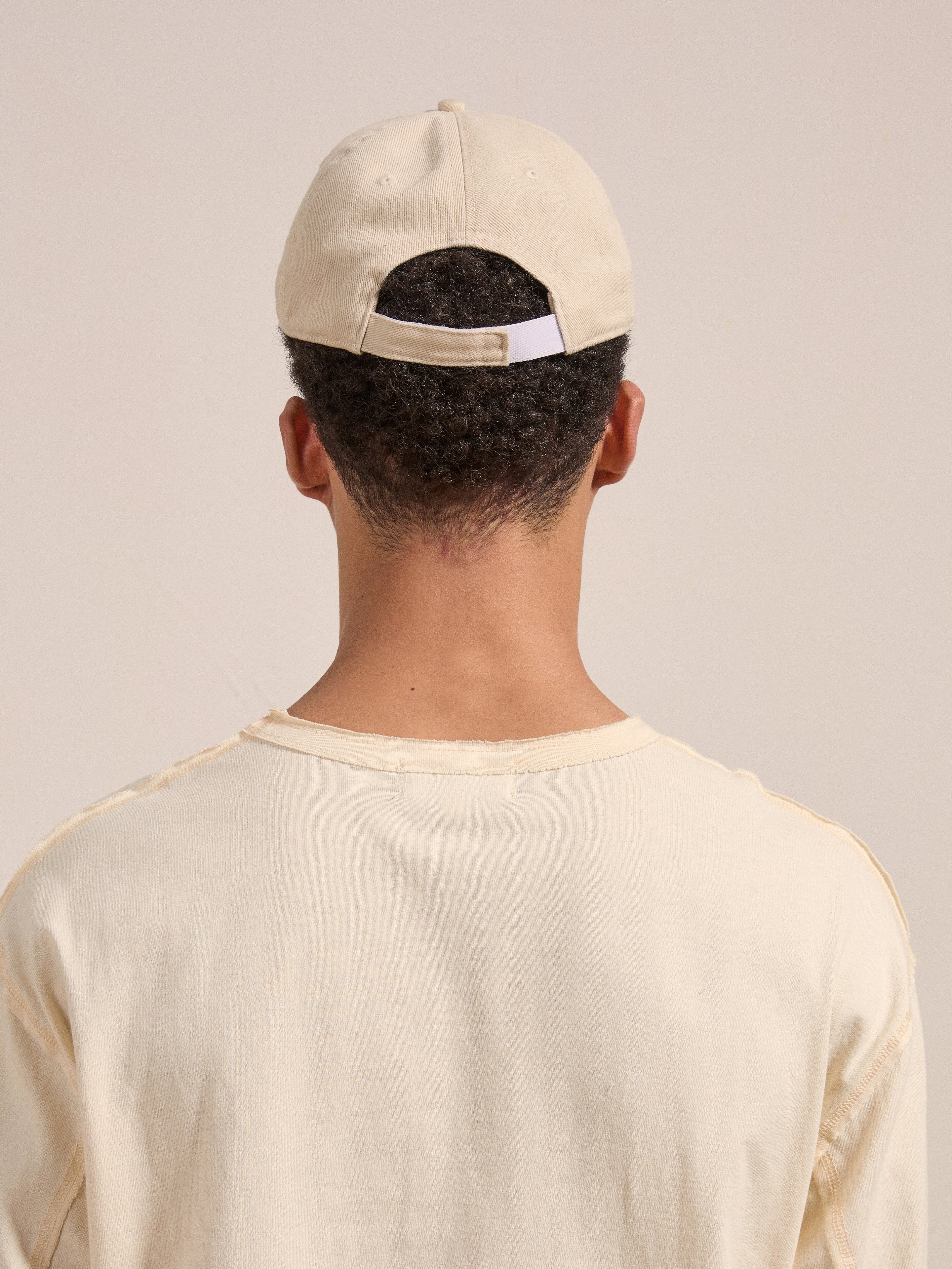 A person wearing an Ivory Felt Patch Cap by FOUND and a light-colored shirt is shown from the back.