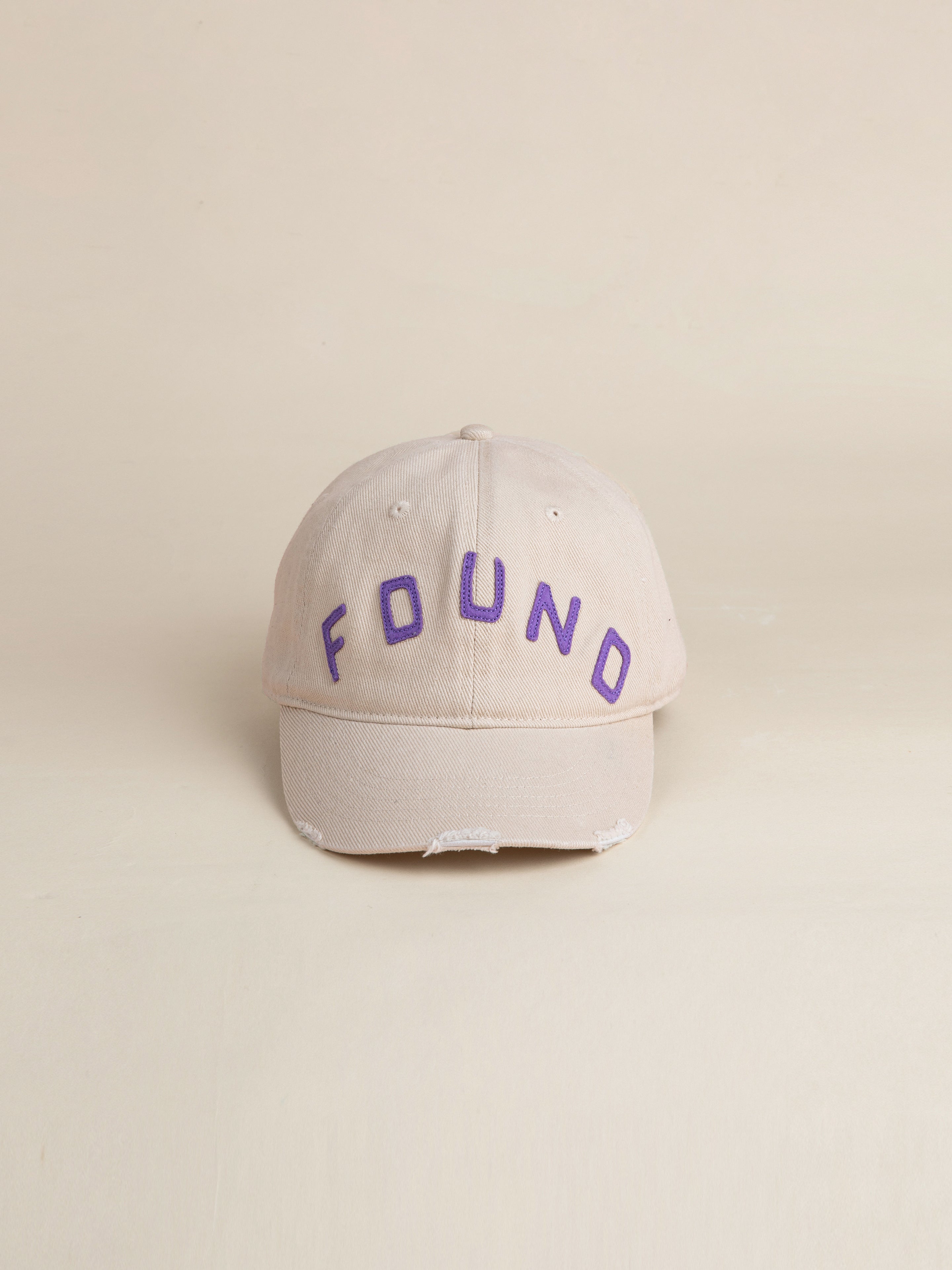 An ivory felt patch cap featuring a vintage washed fabric 6-panel design with a curved brim and the brand name "FOUND" embroidered in purple on the front.