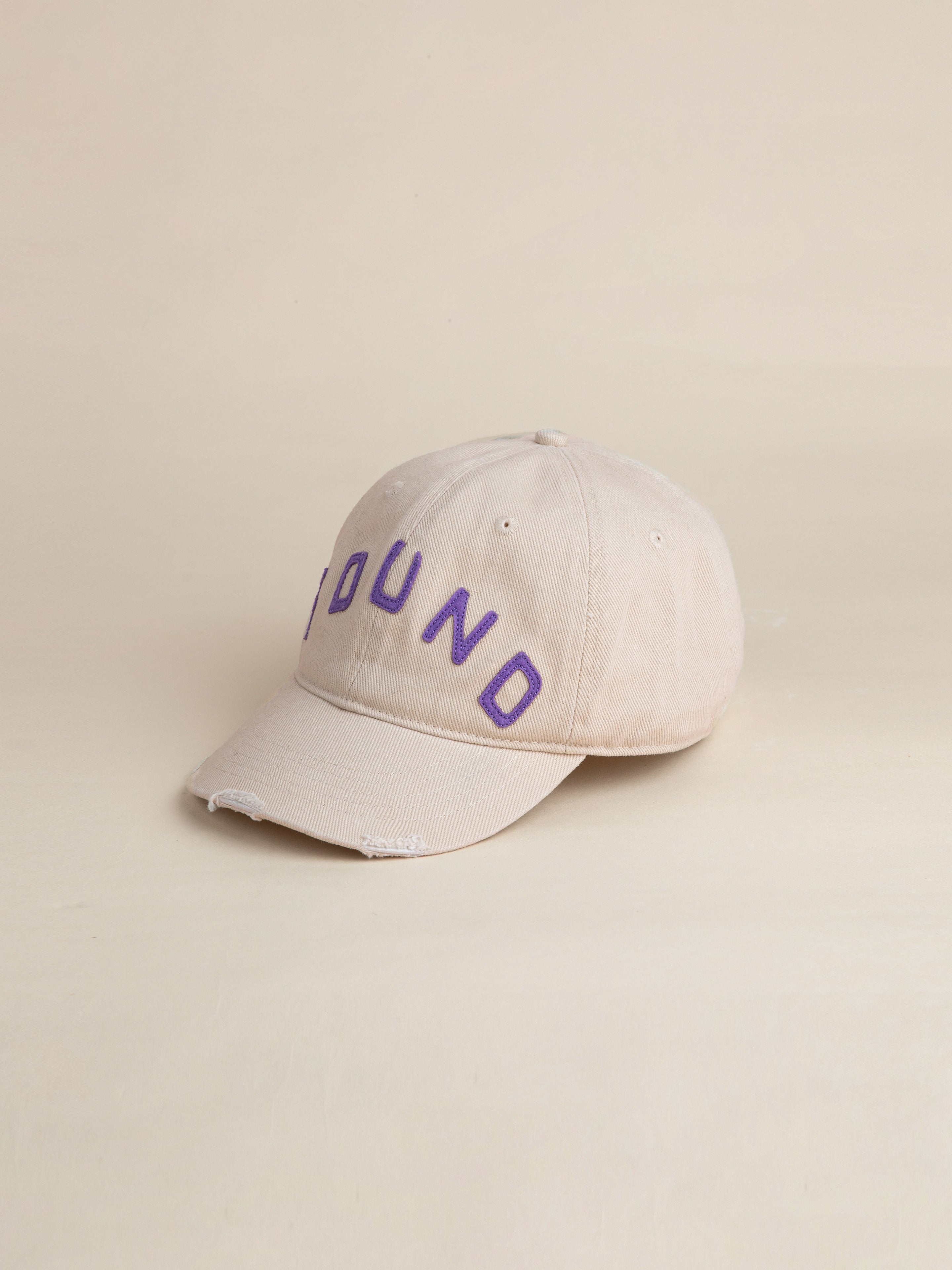 Introducing the Ivory Felt Patch Cap by FOUND: a vintage washed fabric beige baseball cap featuring "FOUND" embroidered in purple on the front. This stylish 6-panel, curved brim cap is perfect for any occasion.