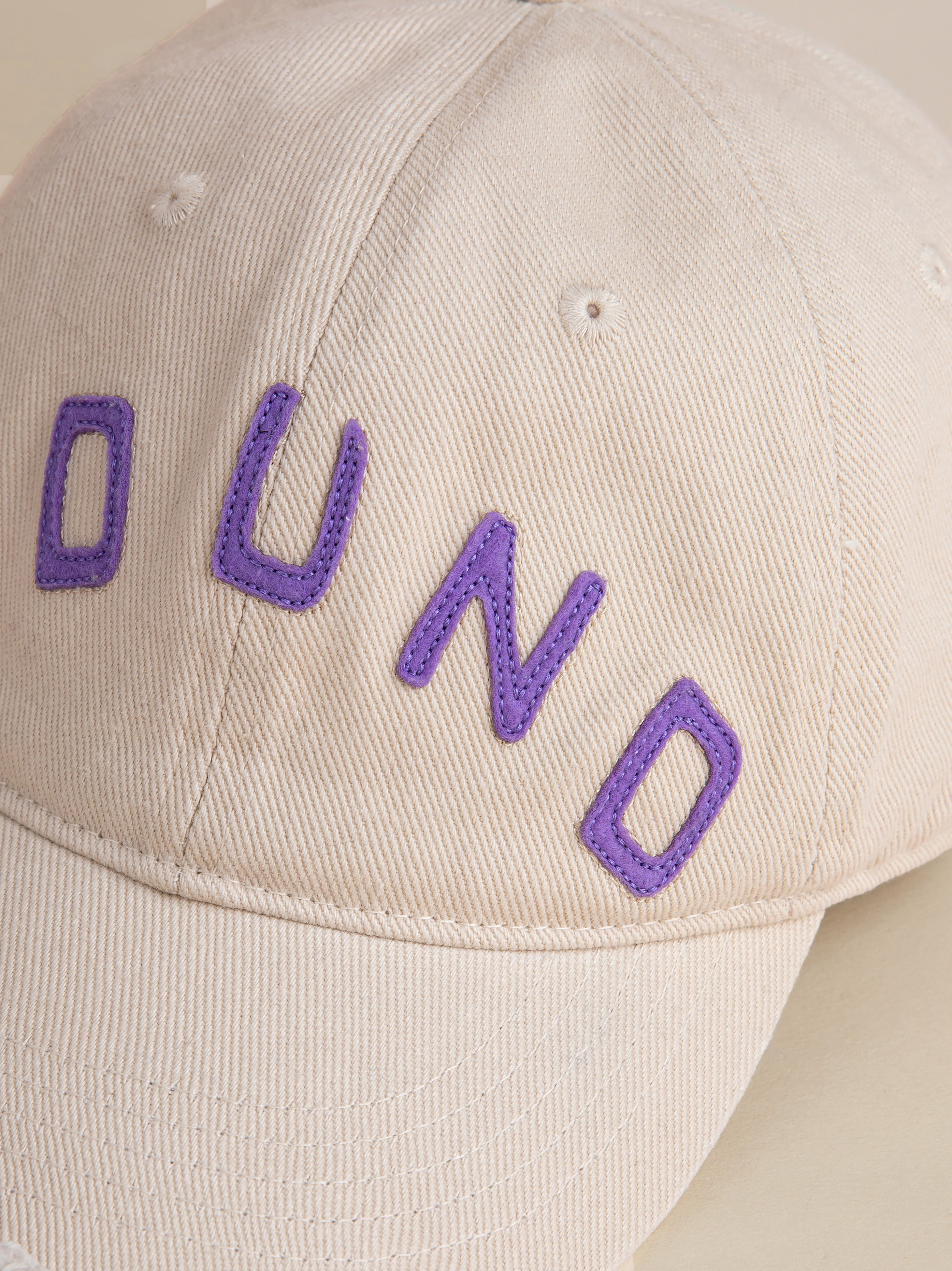 Introducing the FOUND Ivory Felt Patch Cap: a classic beige, 6-panel curved brim cap with vintage washed fabric and "OUND" embroidered in purple on the front.