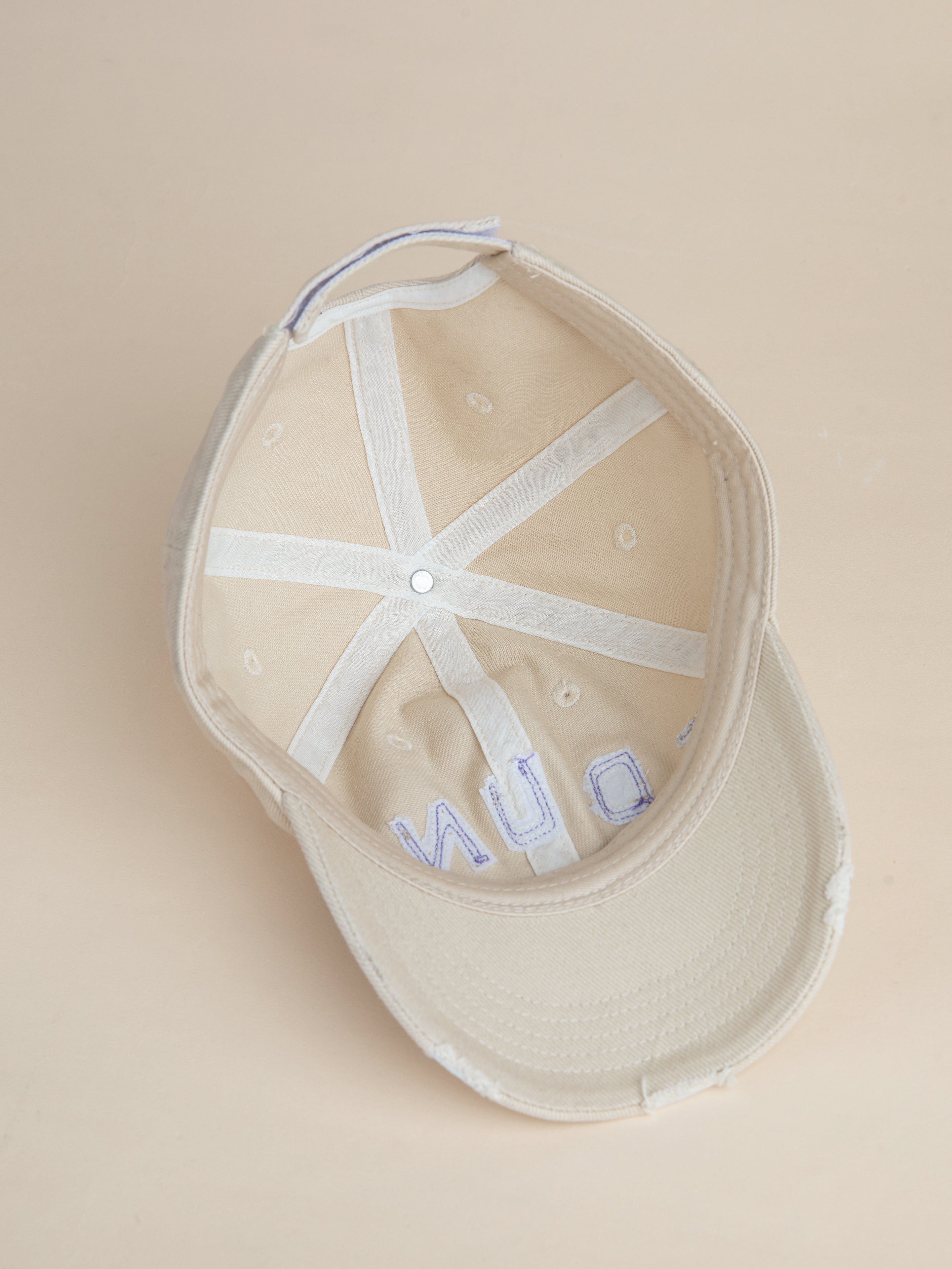 An inside-out look at the Ivory Felt Patch Cap by FOUND reveals its inner stitching and structure. The 6-panel curved brim highlights the meticulous craftsmanship, with visible fabric and seams, as well as a faint text partially seen near the brim.