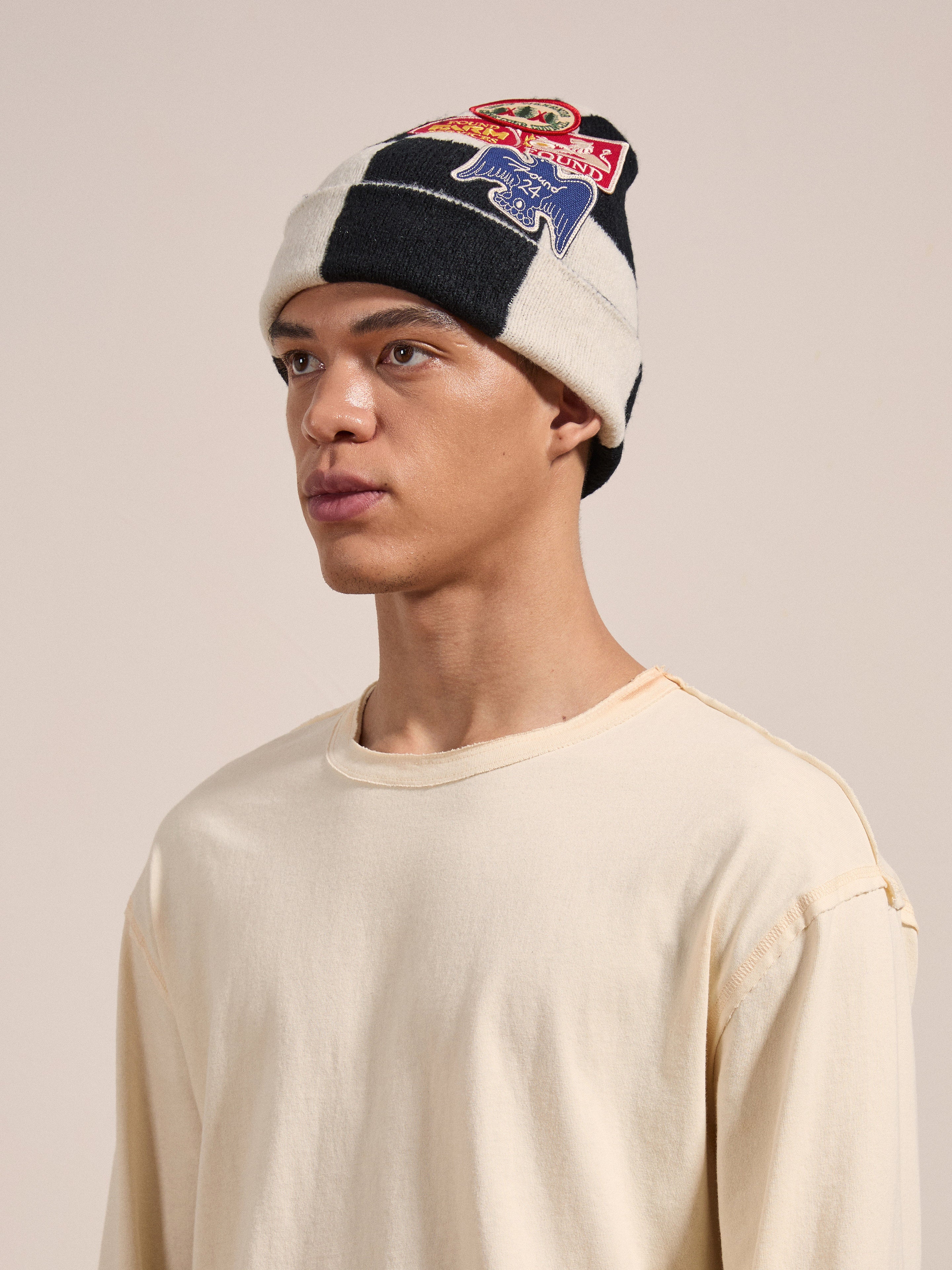 A person wearing a cream-colored long-sleeve shirt and FOUND's Check Multi Patch Beanie stands against a plain backdrop.