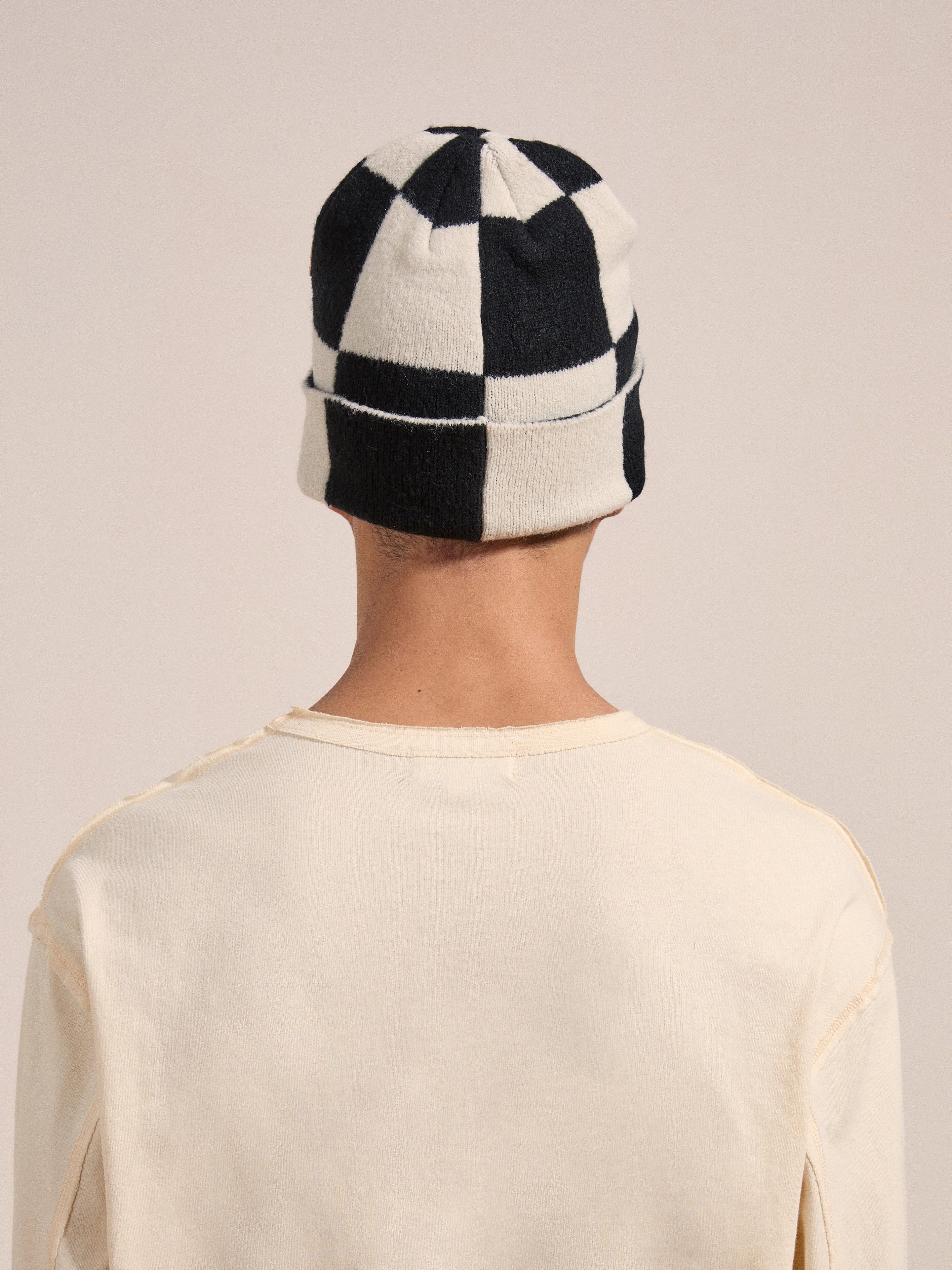 A person wearing a cream-colored shirt and the FOUND Check Multi Patch Beanie is seen from the back against a plain background.