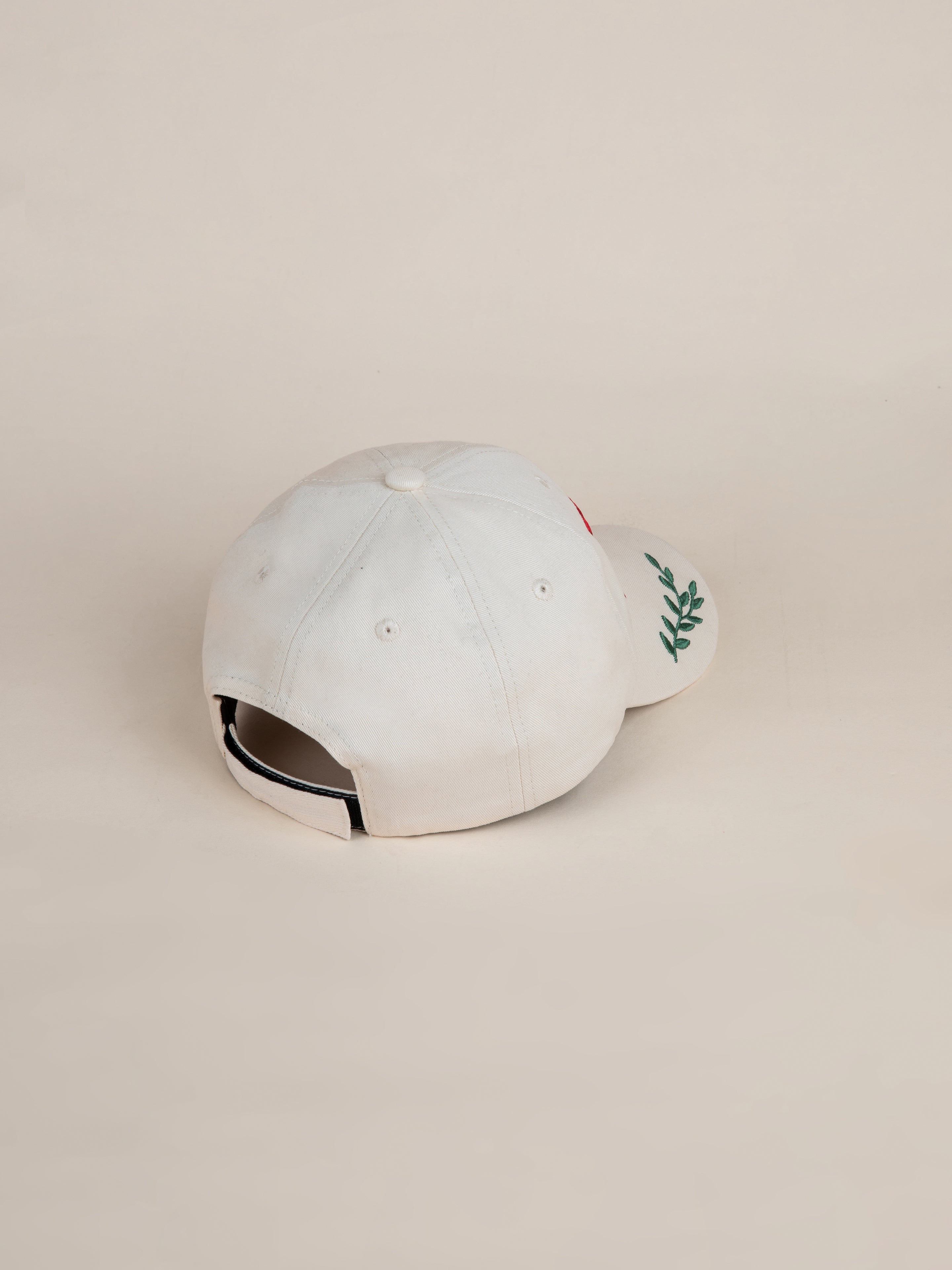 The Jockey Club Found Cap by FOUND, featuring a white color with a leafy green design and the subtle integration of the FOUND logo on the front, showcases an ideal combination of style and craftsmanship when viewed from the back.