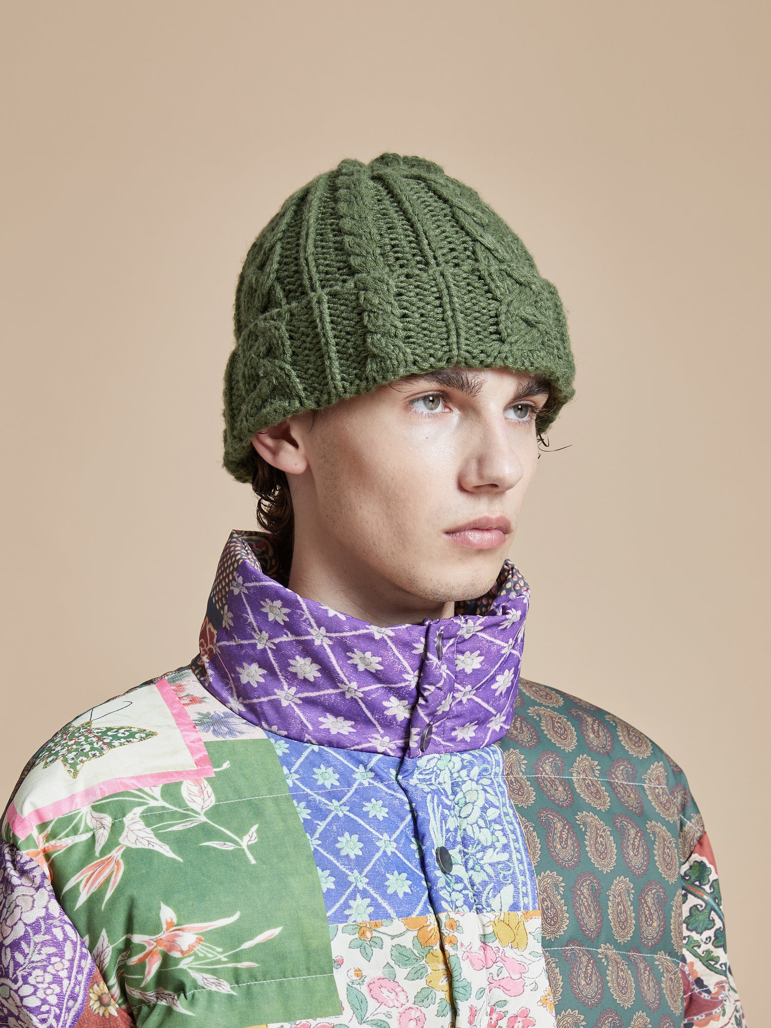 A man wearing a Profound Forest Cable Knit Beanie and patchwork jacket.