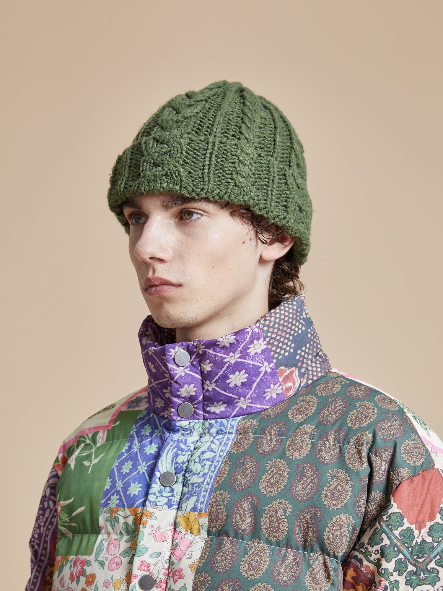 A man wearing a Profound Forest Cable Knit Beanie with a patchwork pattern.