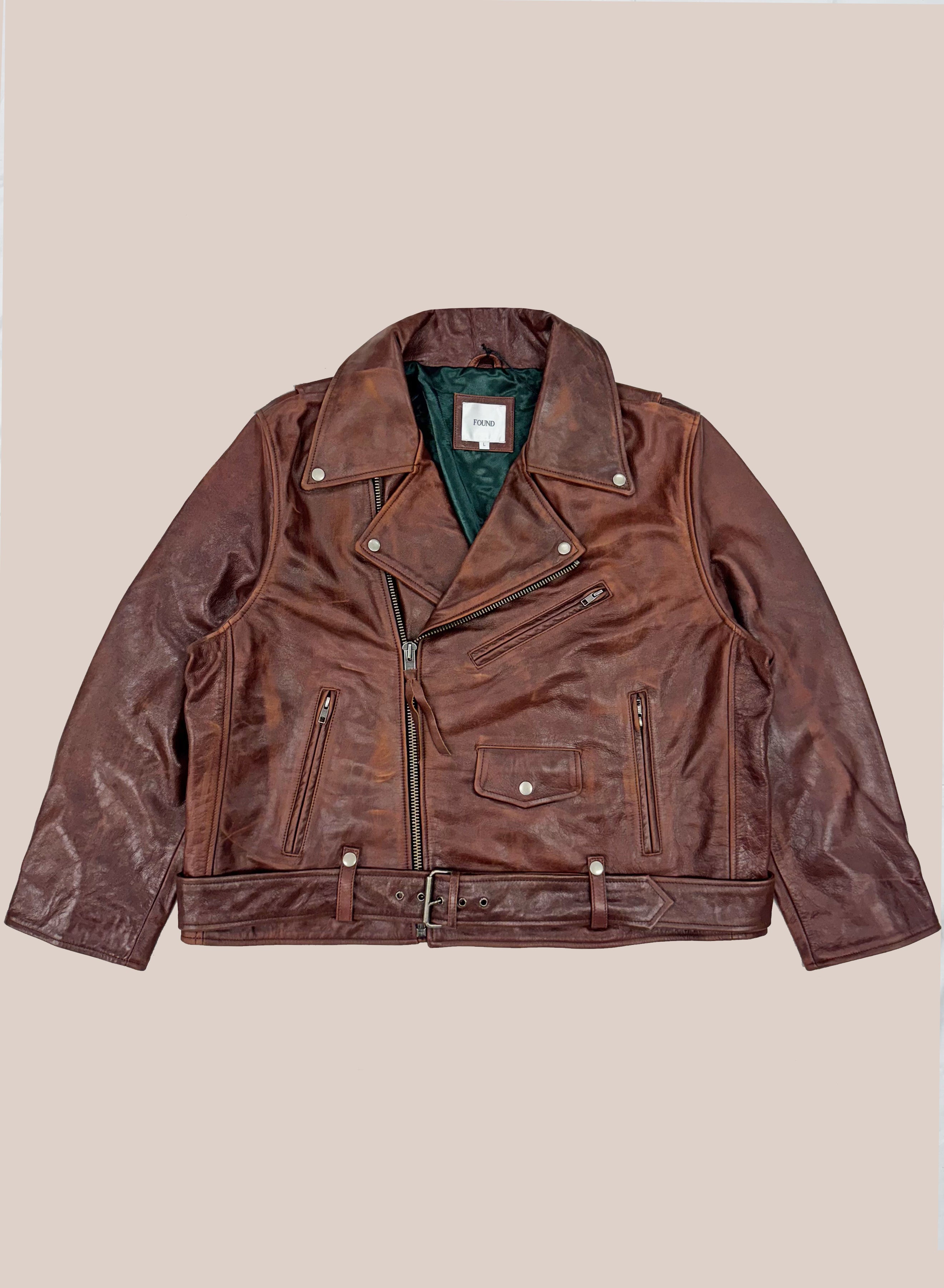 The FOUND Leather Biker Jacket is a brown unisex style featuring an asymmetrical zipper, multiple pockets, and a waist belt, shown laid flat on a neutral background.