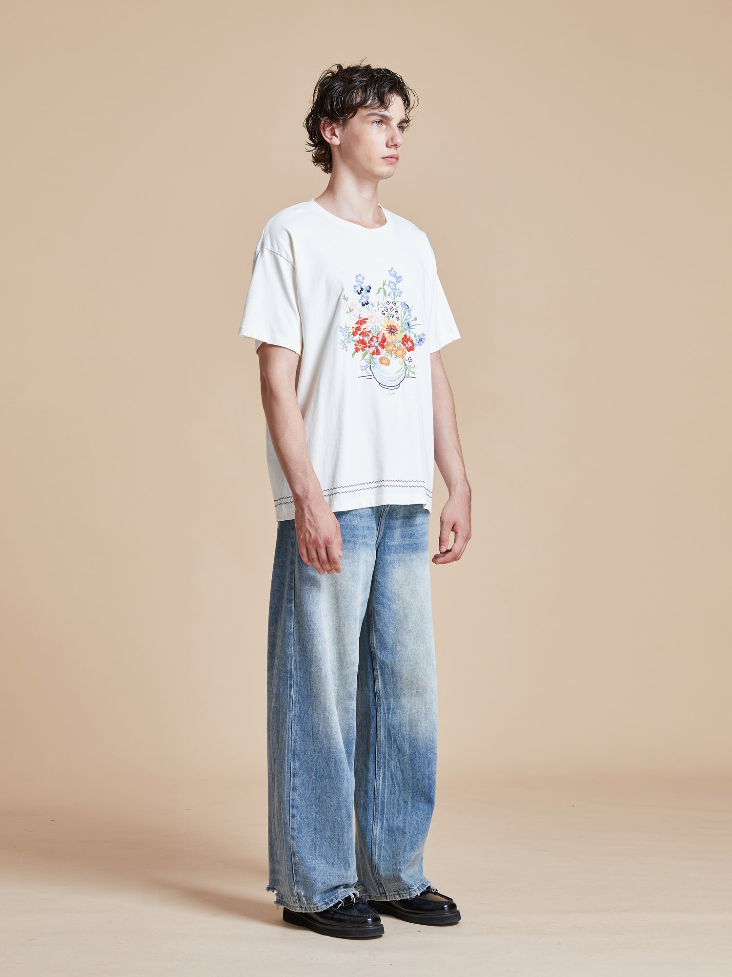 A man wearing a Found Bouquet Flowers Tee and blue jeans.