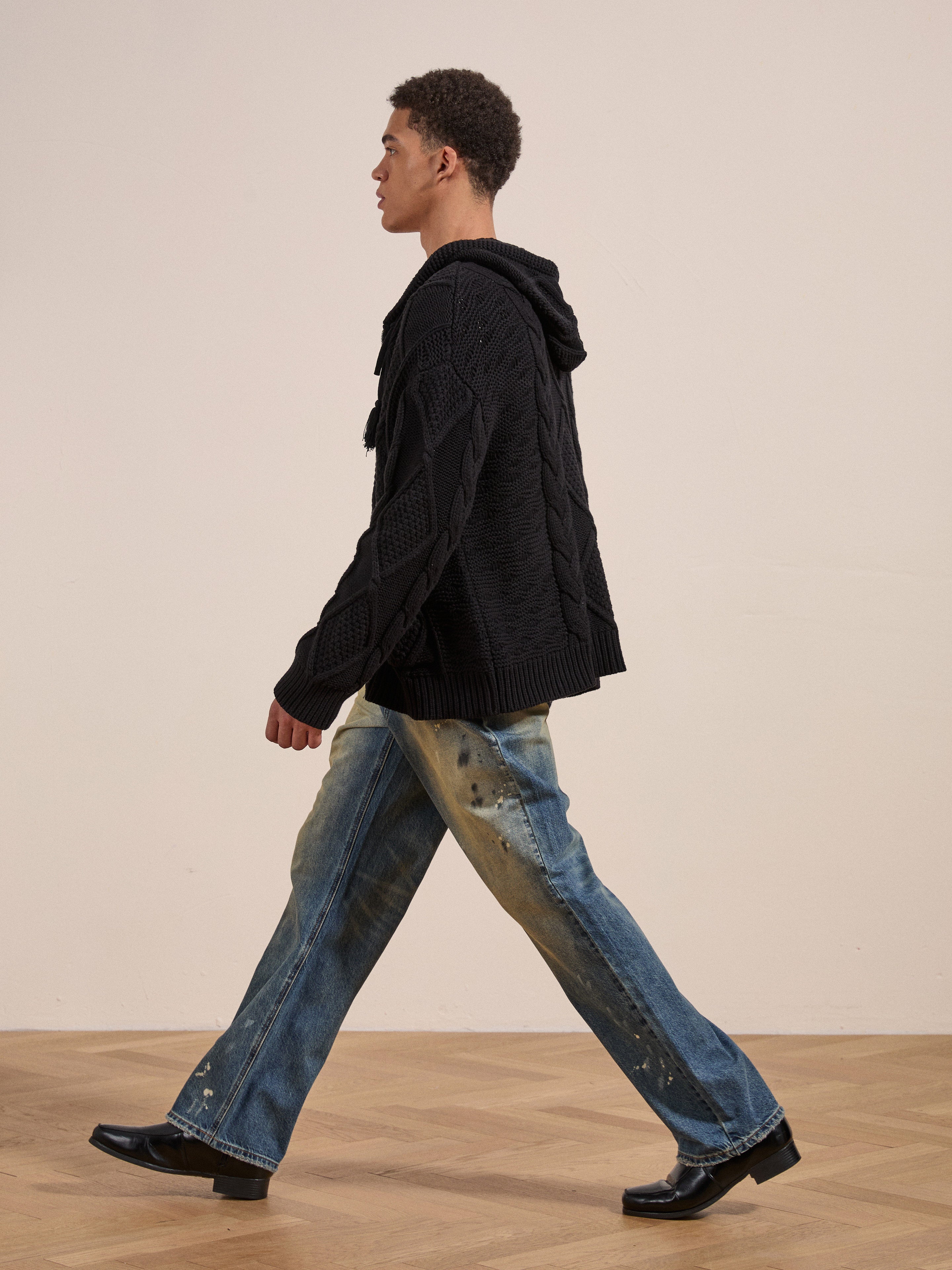 A person wearing the Zip Up Cable Knit Hoodie by Found and blue jeans walks across a wooden floor, facing left, showcasing a cozy look and feel.