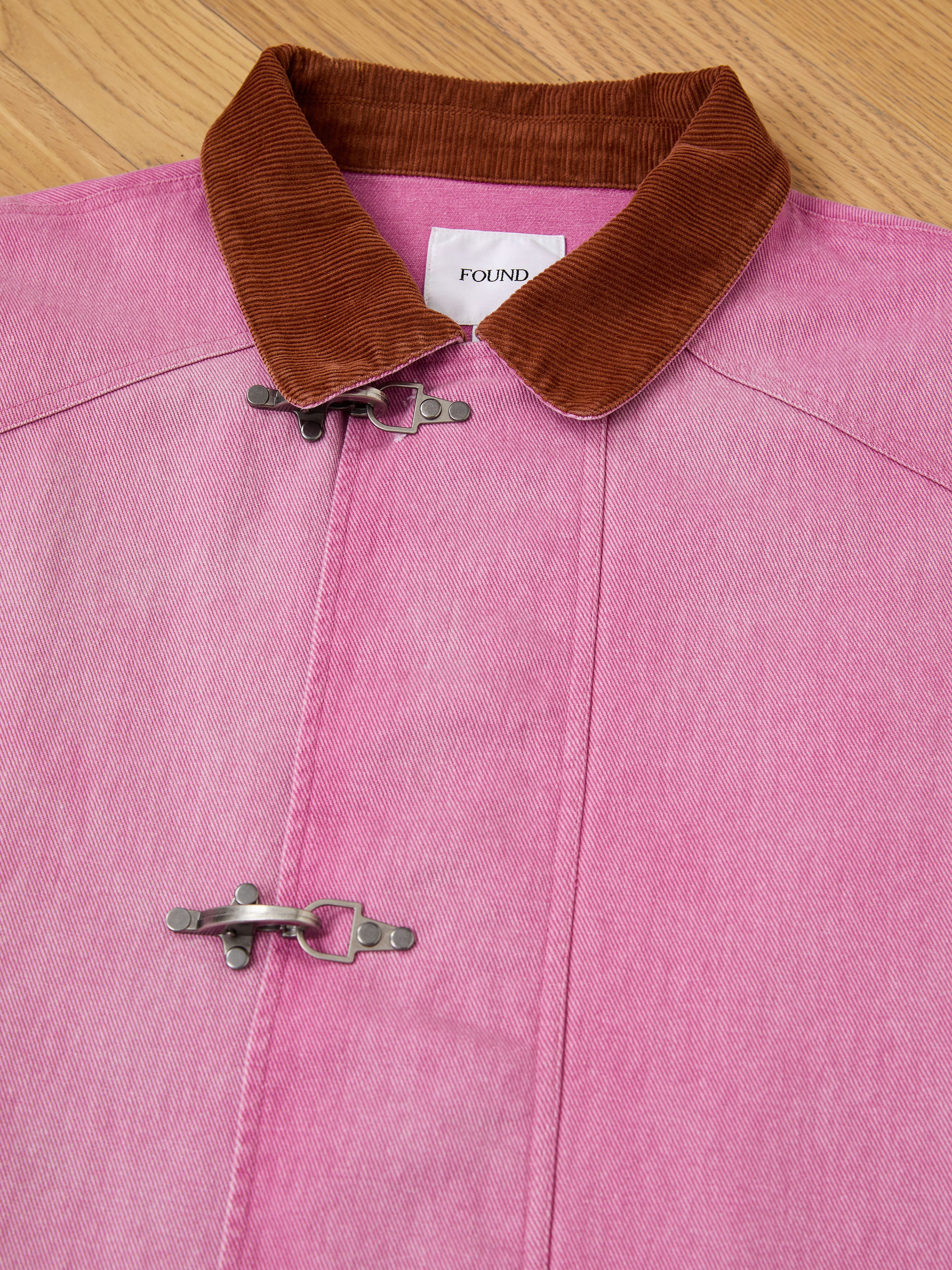 The Washed Fireman Clasp Workshop Jacket by Found features a pink finish, brown corduroy collar, two metal latch closures, and a visible white "FOUND" label, displayed flat on a wooden surface.