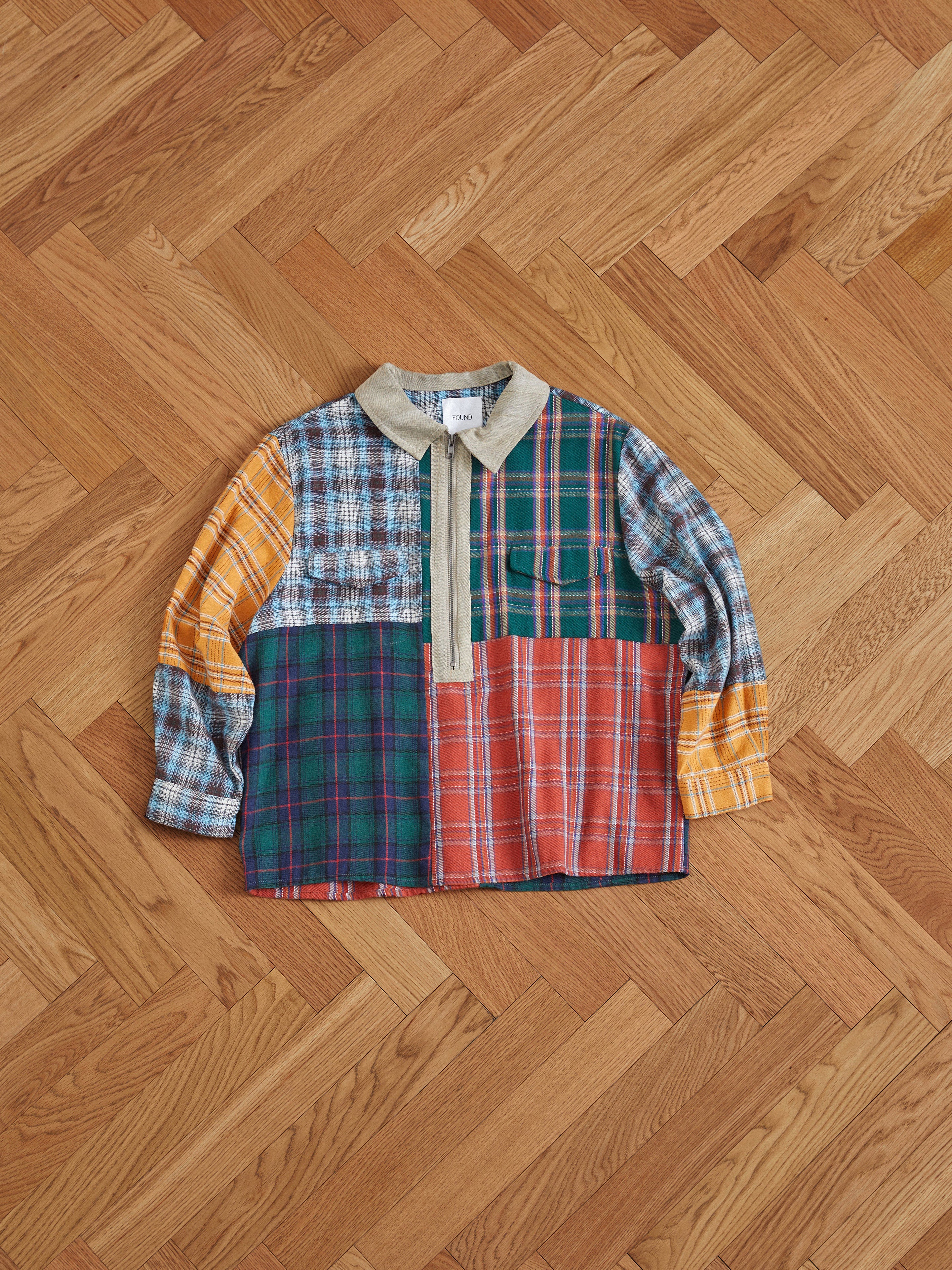 A Found Multi Plaid Tartan Shirt with handcrafted distressing laying on a wooden floor.