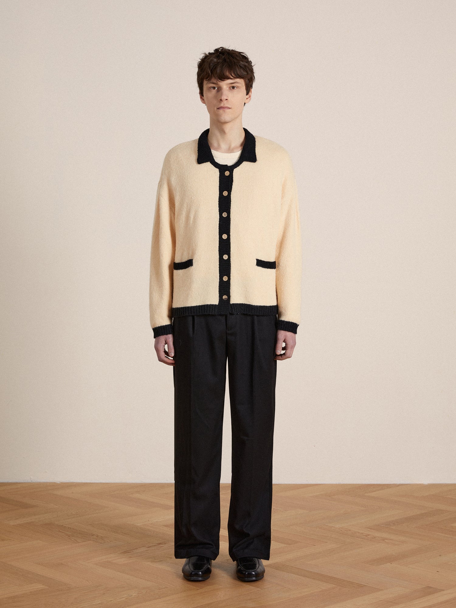 A man wearing a Found Sima Contrast Collar Knitted Cardigan with wooden buttons and black pants.