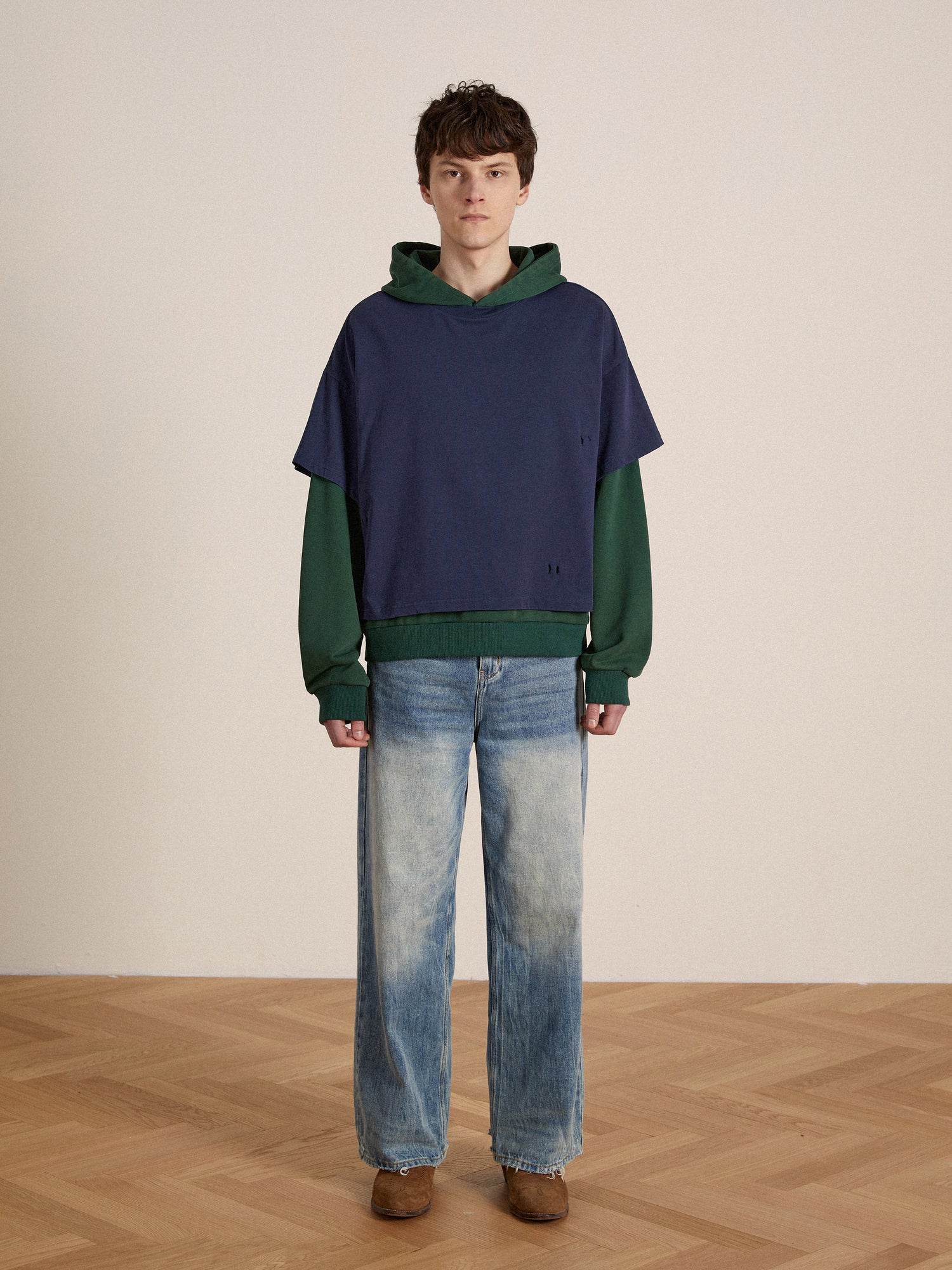 A man wearing a Found double layer hoodie and lacy baggy jeans standing on a wooden floor.