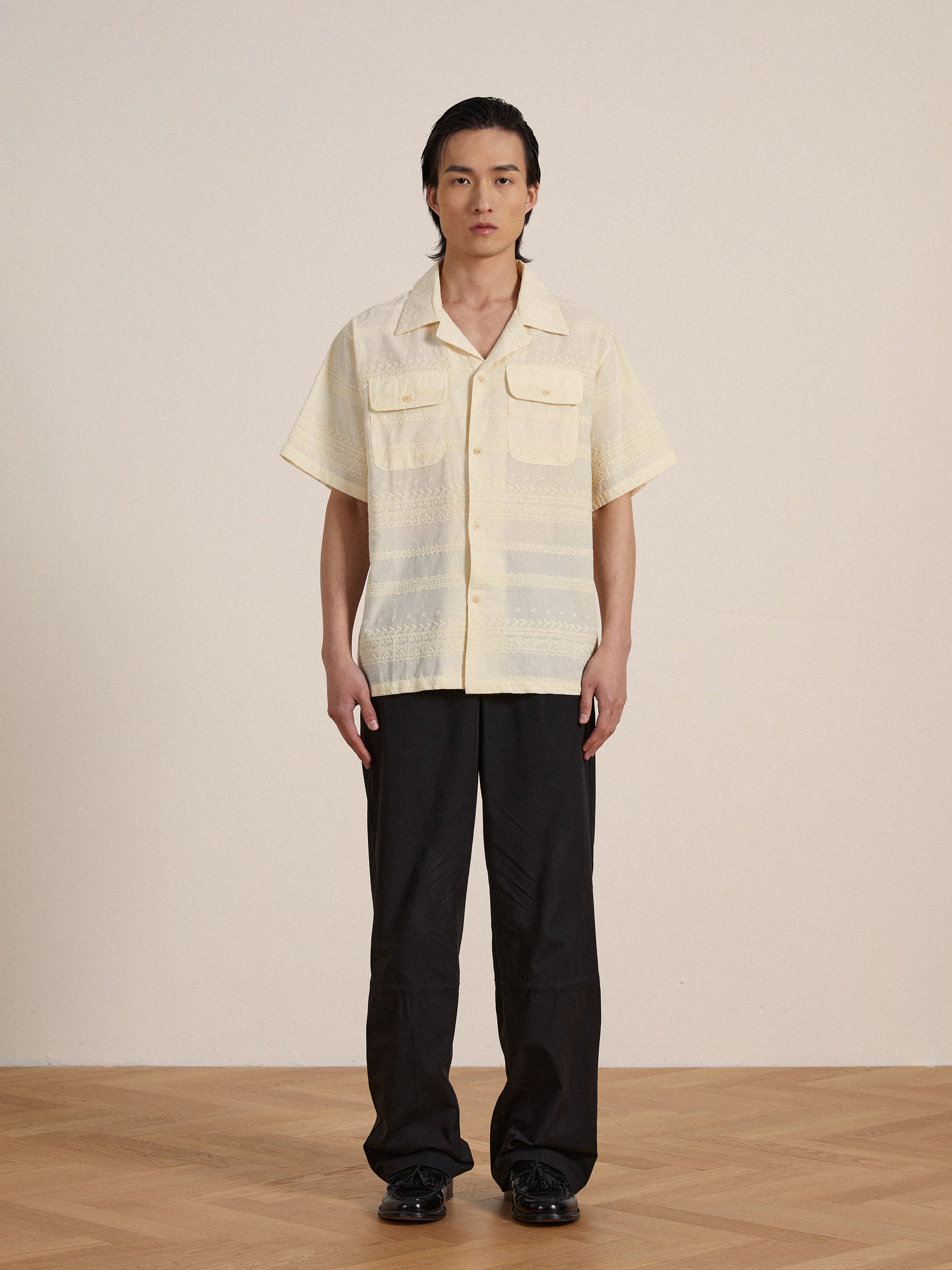 A man wearing a yellow Found Lace SS Camp Shirt with delicate lace detailing and black pants.