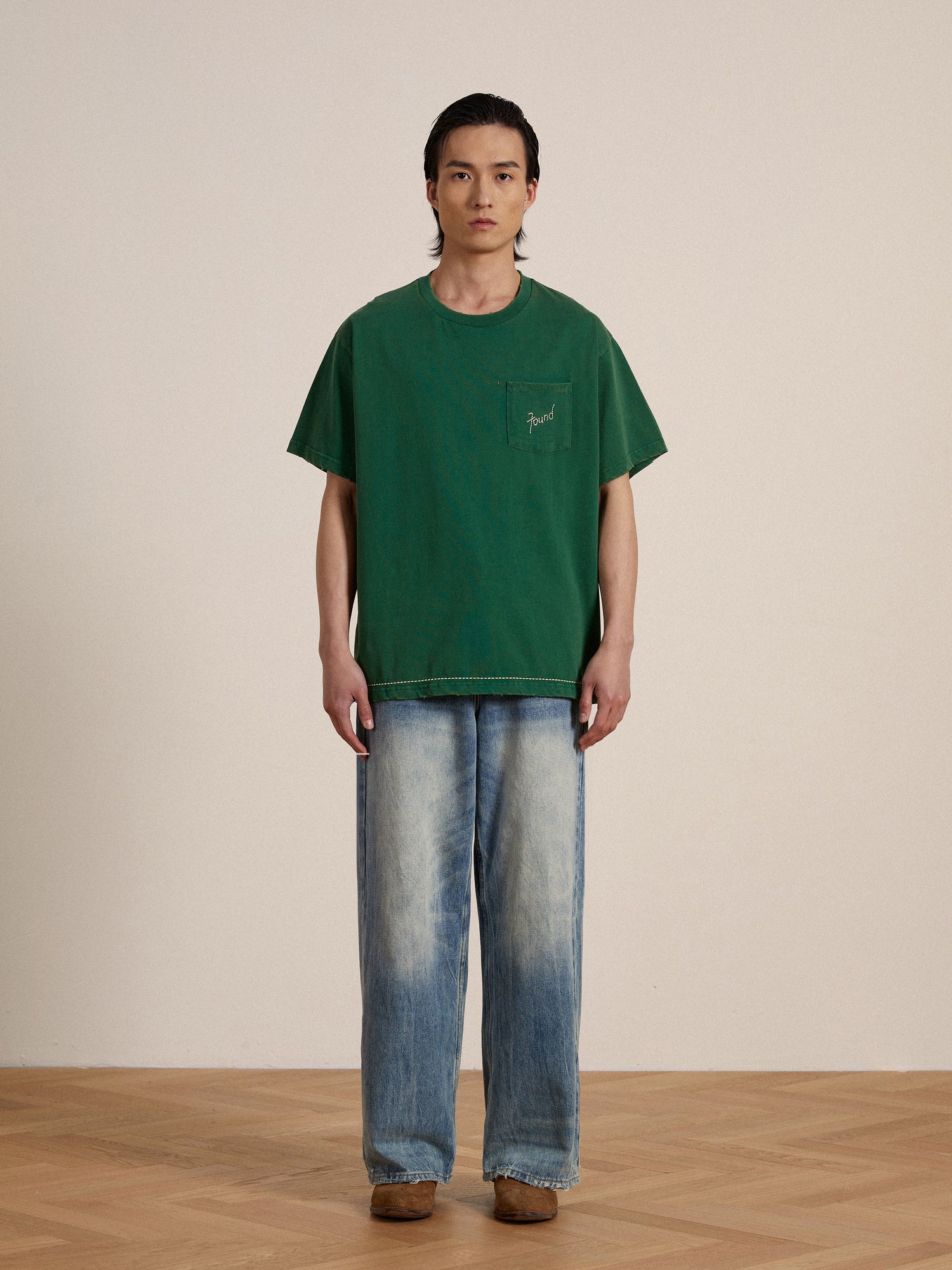 A man wearing a green Found Embroidered Logo Tee and jeans.