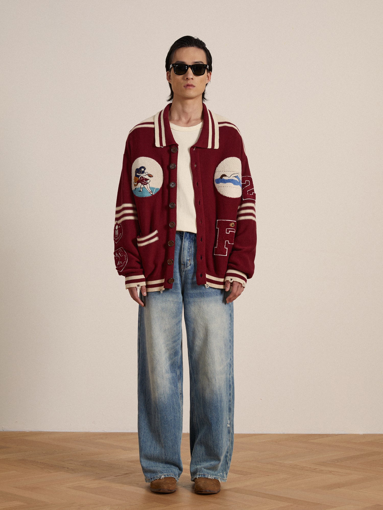 A man wearing a burgundy Found Varsity Patch Collared Cardigan and jeans, reflecting vintage Ivy League fashion.