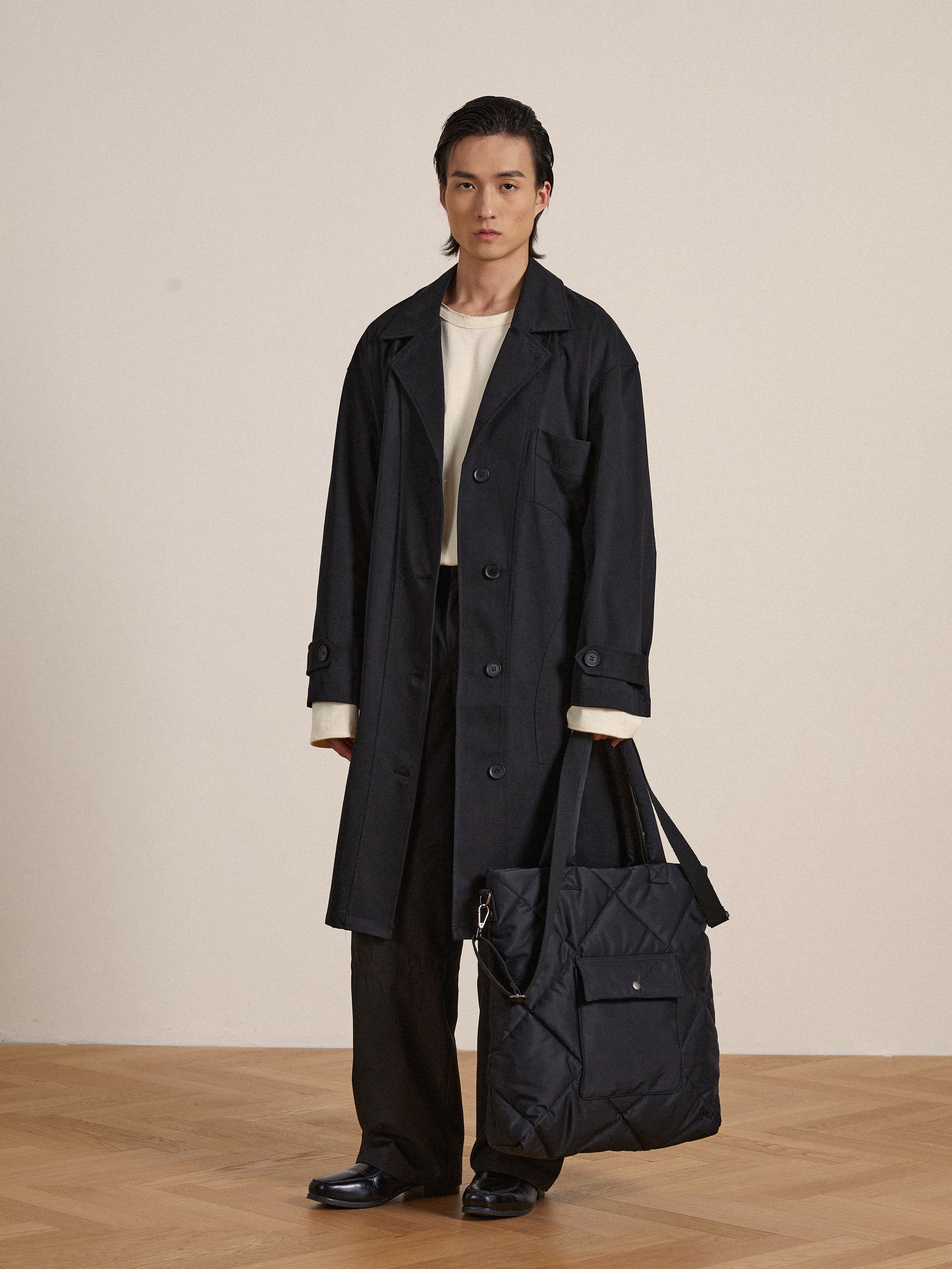 A man in a trench coat holding a Profound Dayer Nylon Quilted Bag.