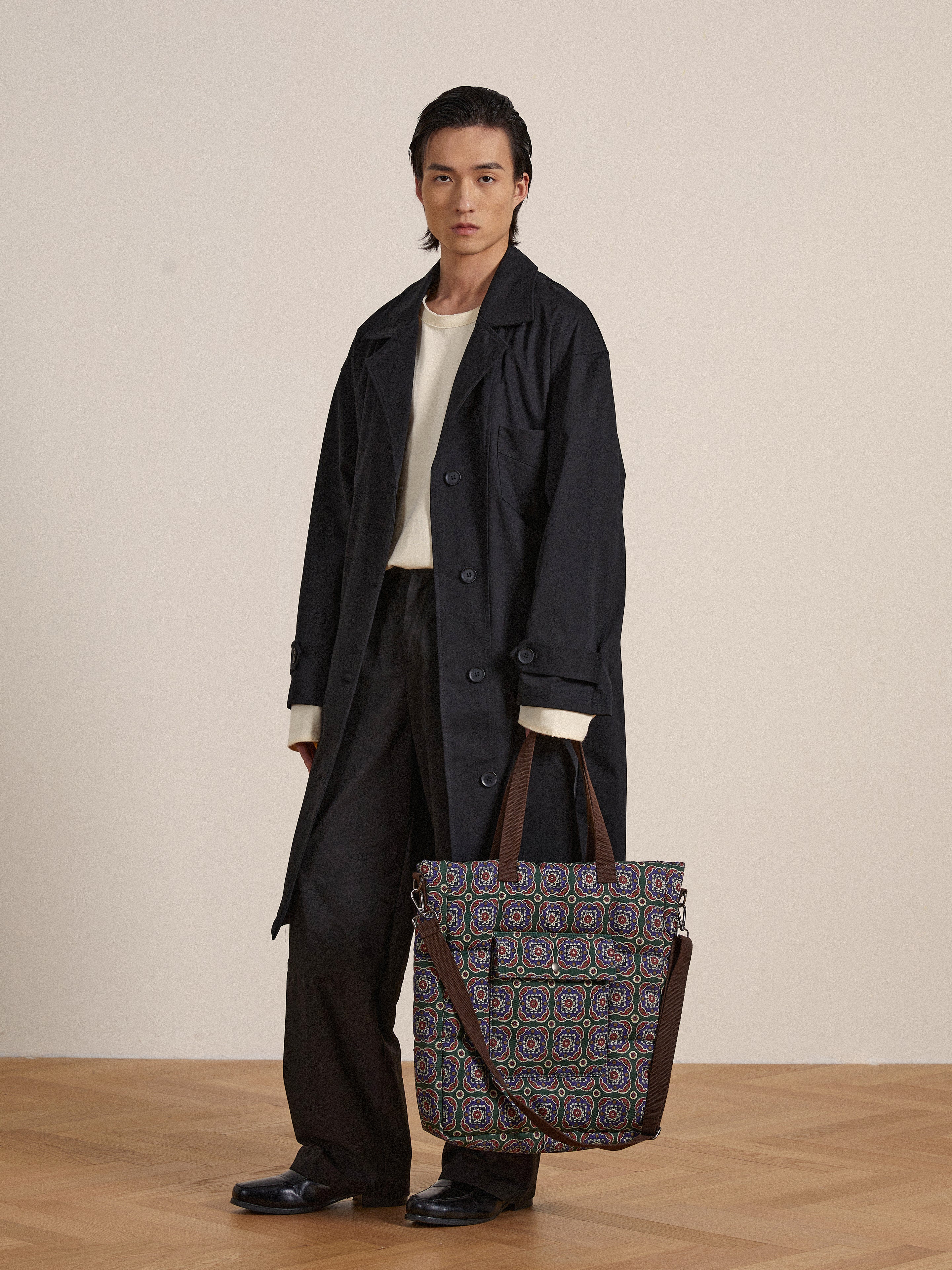 A man in a trench coat holding a Profound Pine Mosaic Bag.