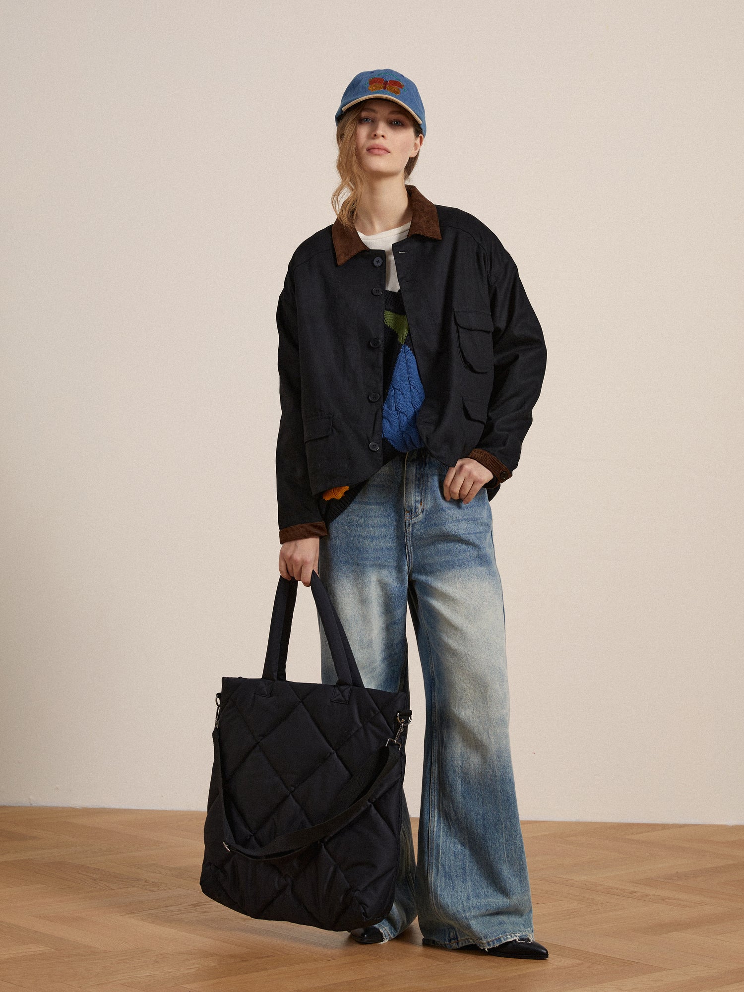 A woman wearing a Lar Waxed Cotton Box Coat by Found and jeans holding a black tote bag.