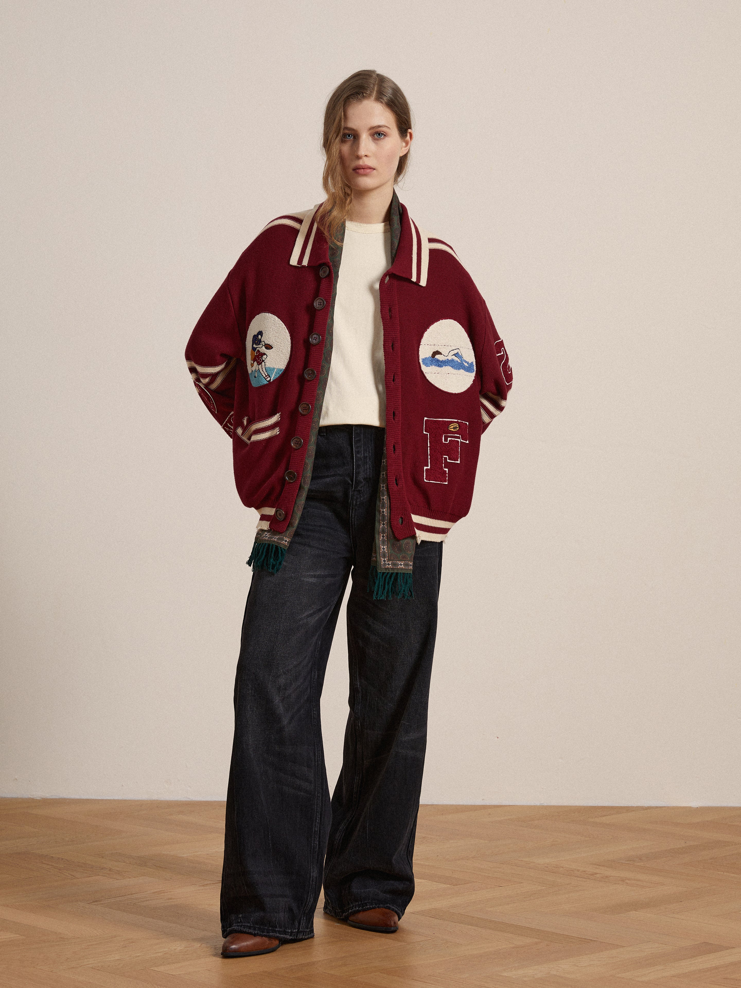 A woman wearing a red bomber jacket with embroidered chenille patches and jeans.