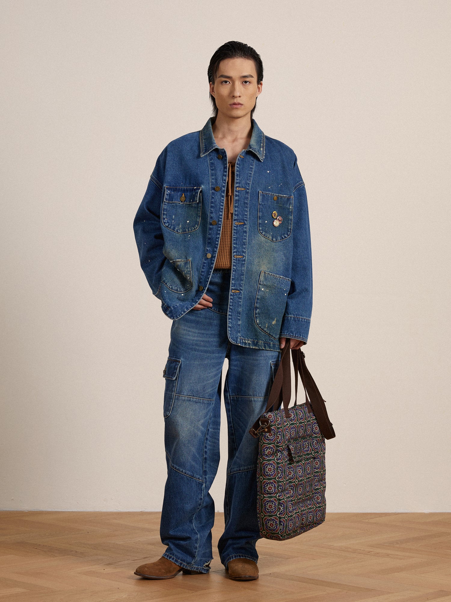 A Kavir Denim Painter Jacket-clad artist in a Found jacket and jeans holding a bag.