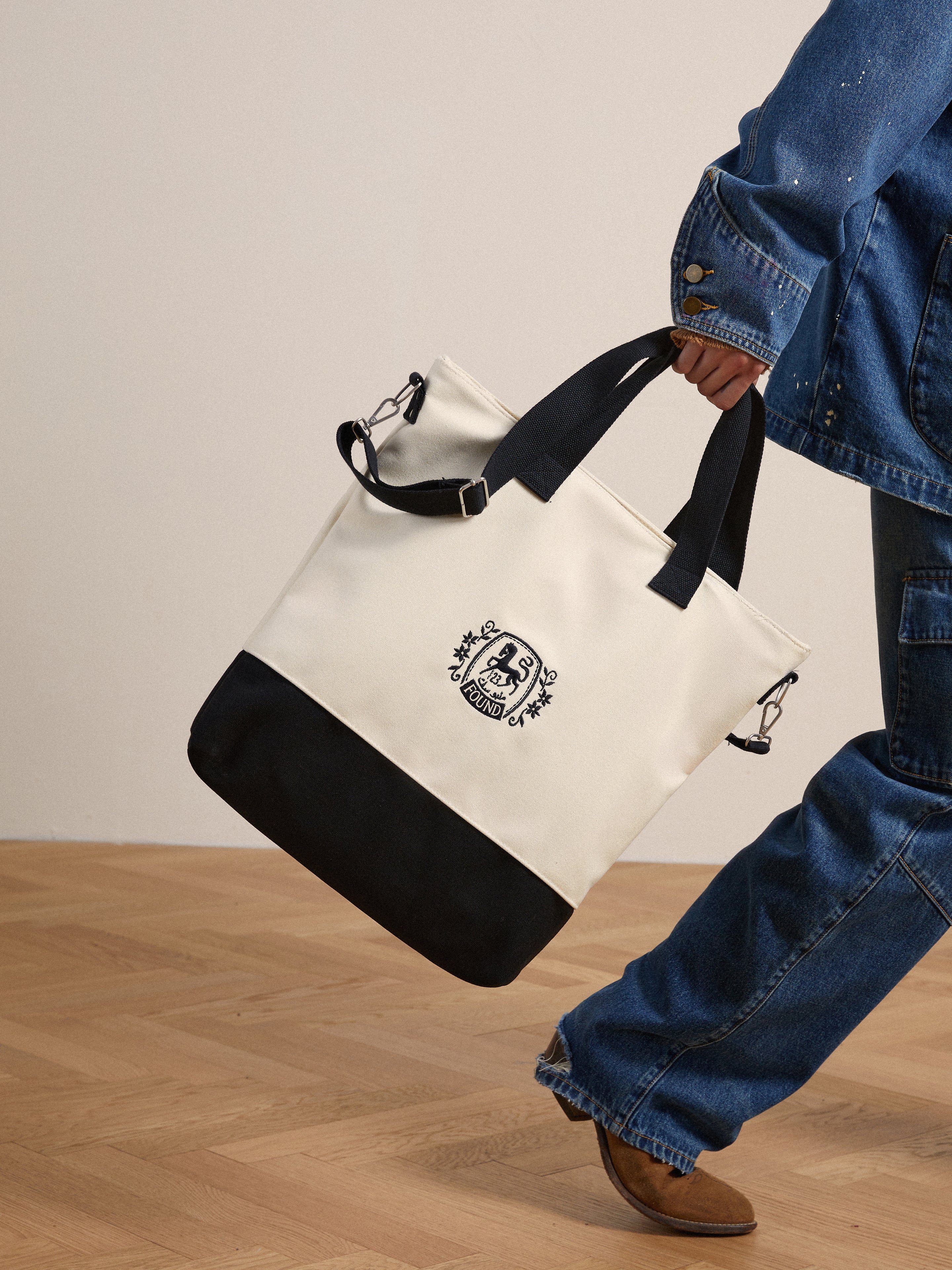 A man is carrying a white and black Profound Horse Logo Crest Canvas Bag.