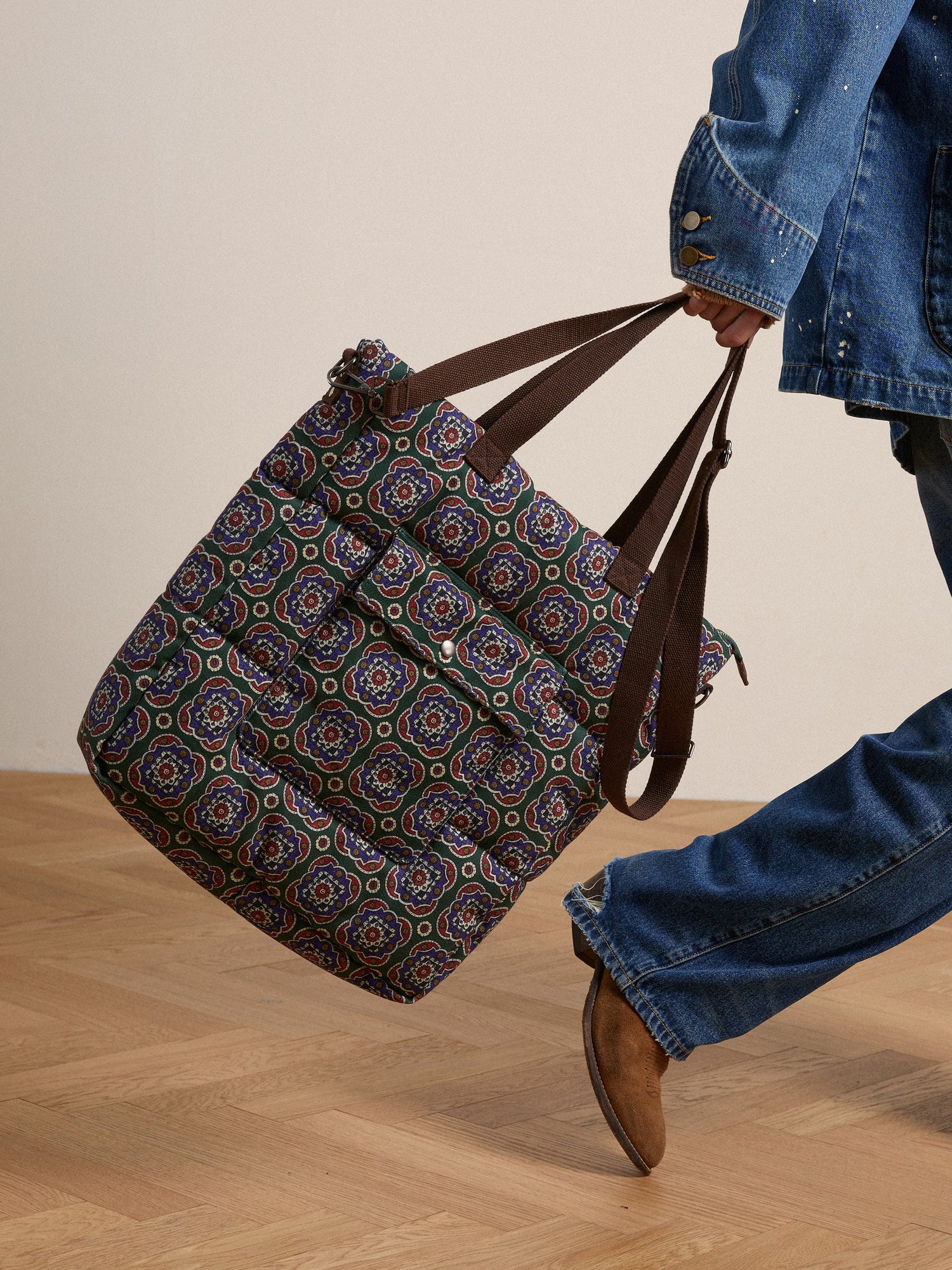A man is carrying a quilted Profound Pine Mosaic Bag with a pattern on it.