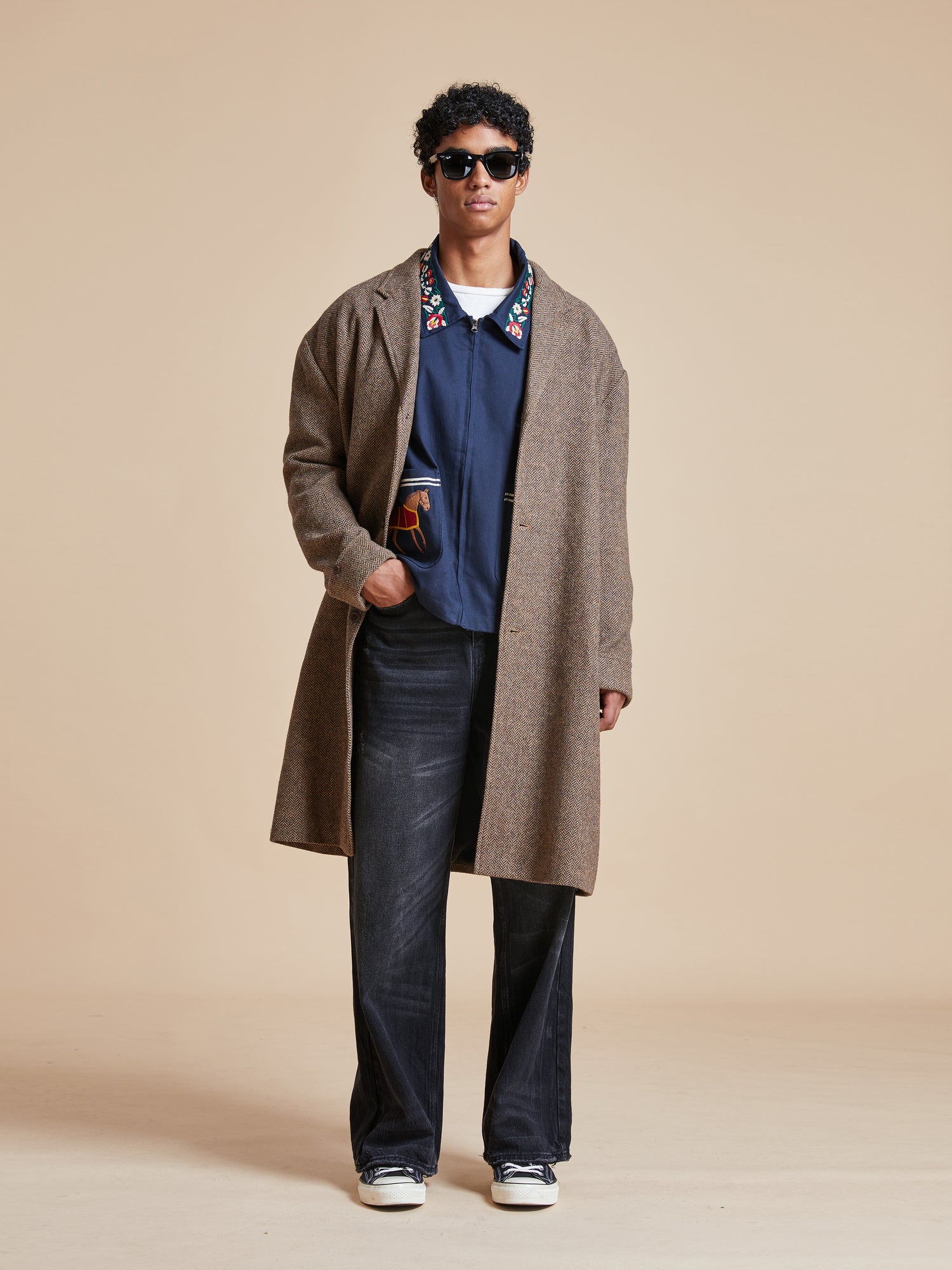 A man in a Found Elm Tweed Long Top Coat and jeans standing on a beige background.