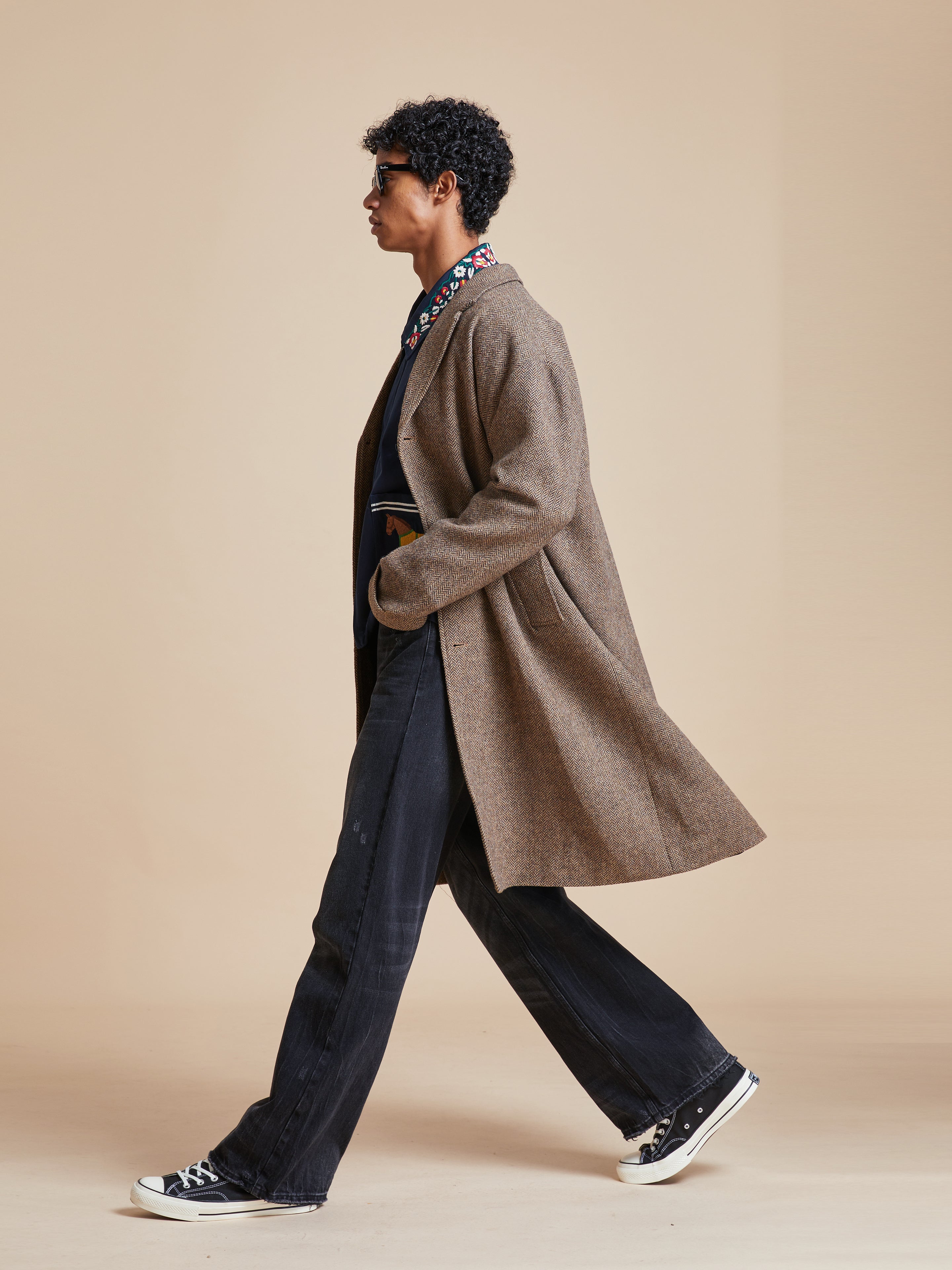 A man in an Elm Tweed Long Top Coat by Found walking on a beige background.